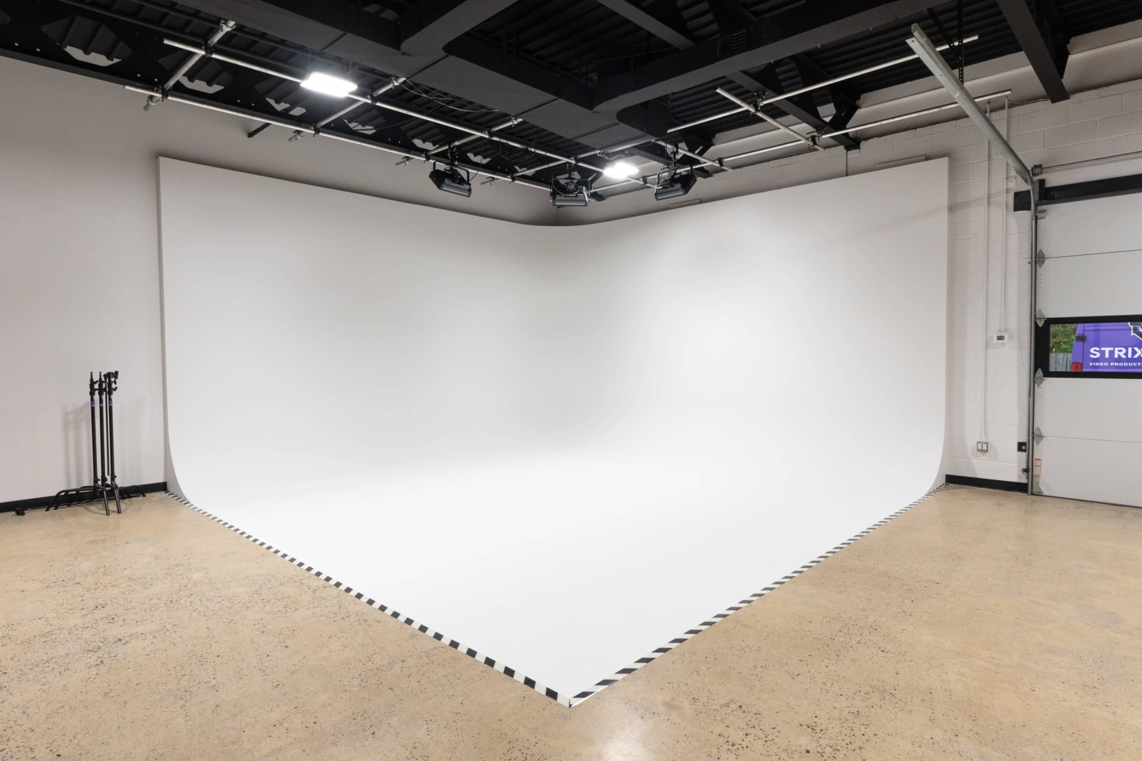 The image shows an empty photography studio with a large, white seamless backdrop and a polished concrete floor.
