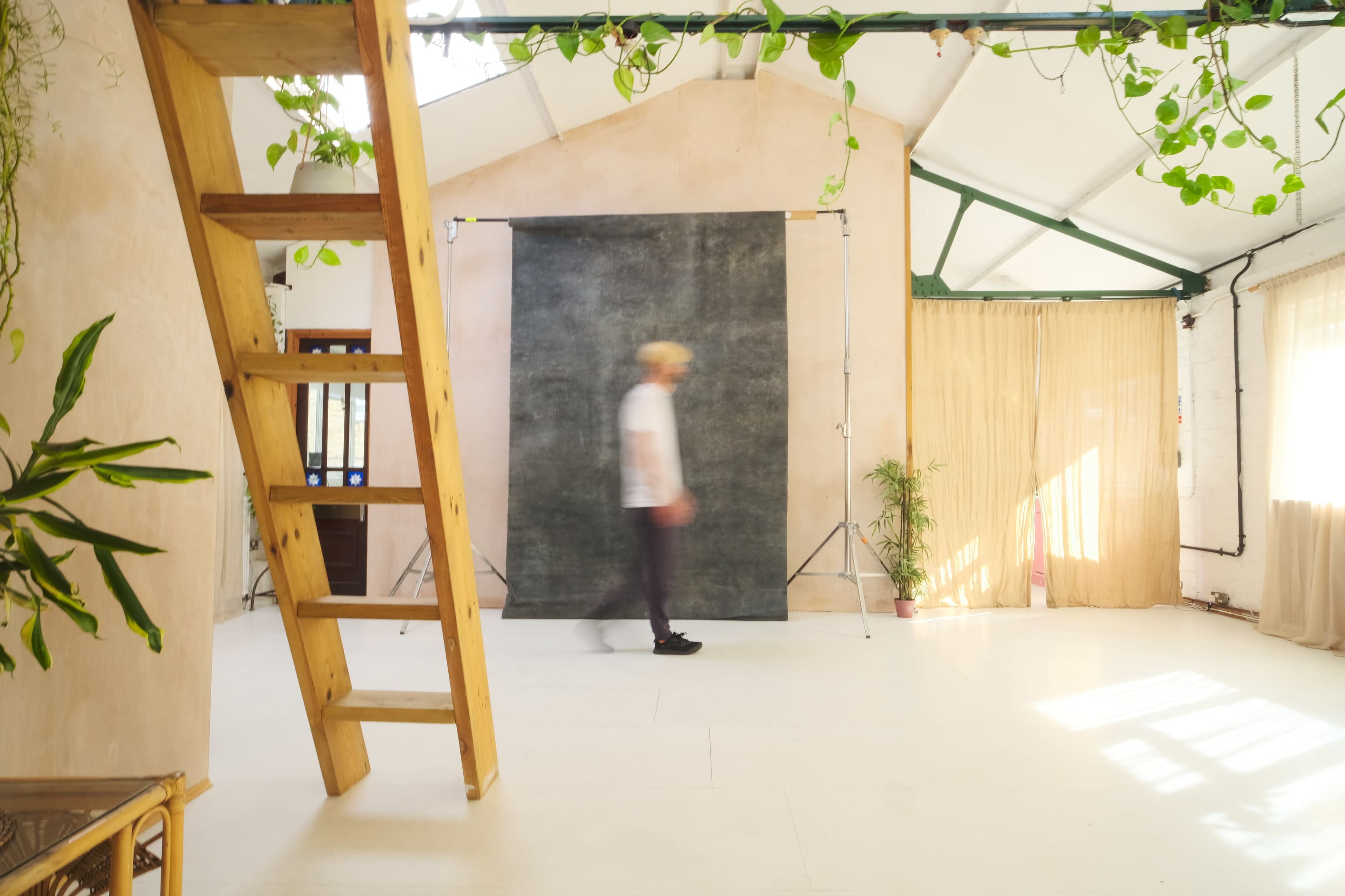 A person walks past a dark backdrop in a minimalist, well-lit studio with wooden elements and greenery.