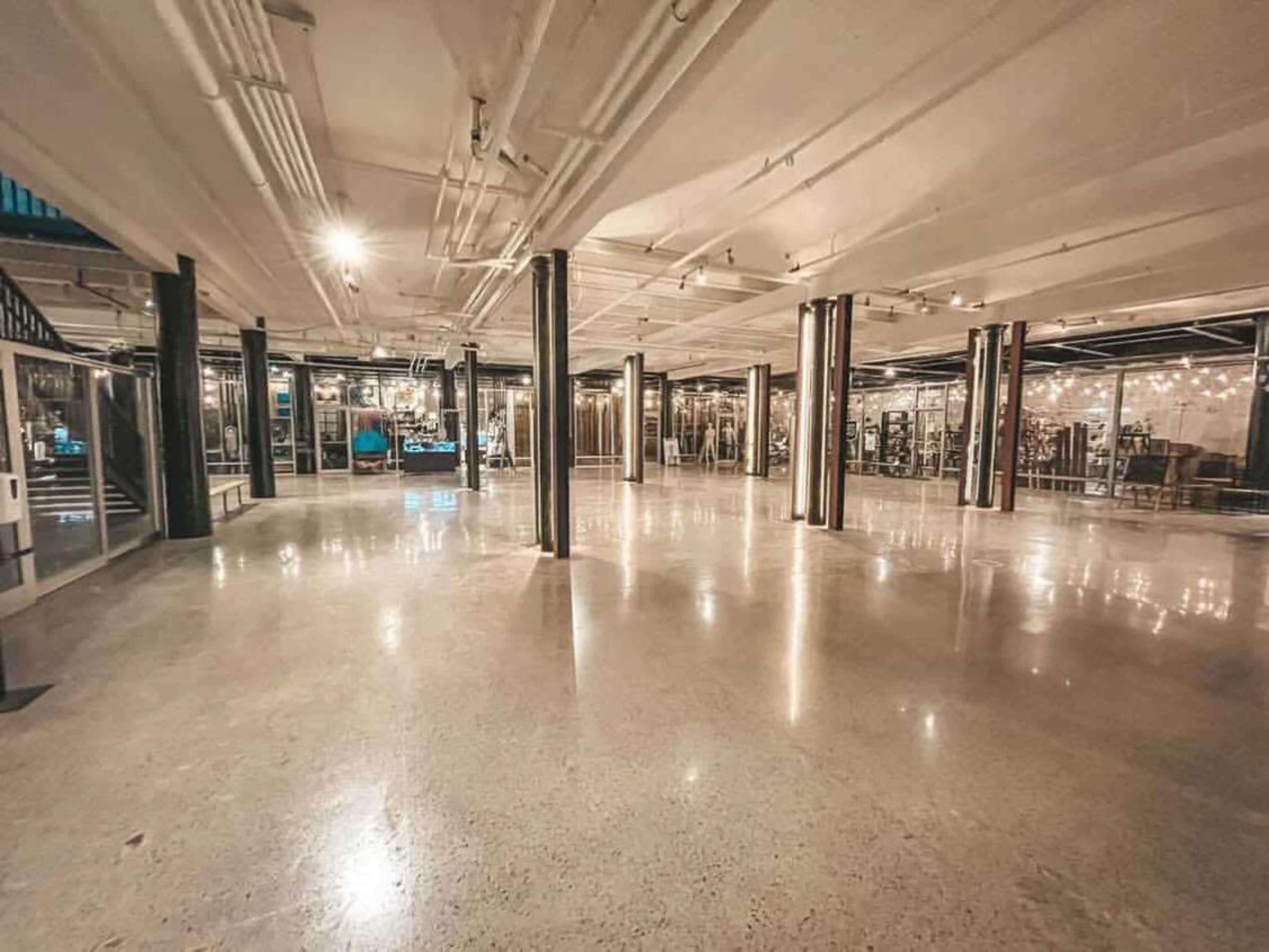 A spacious, empty industrial-style interior with polished concrete floors and exposed pipes.