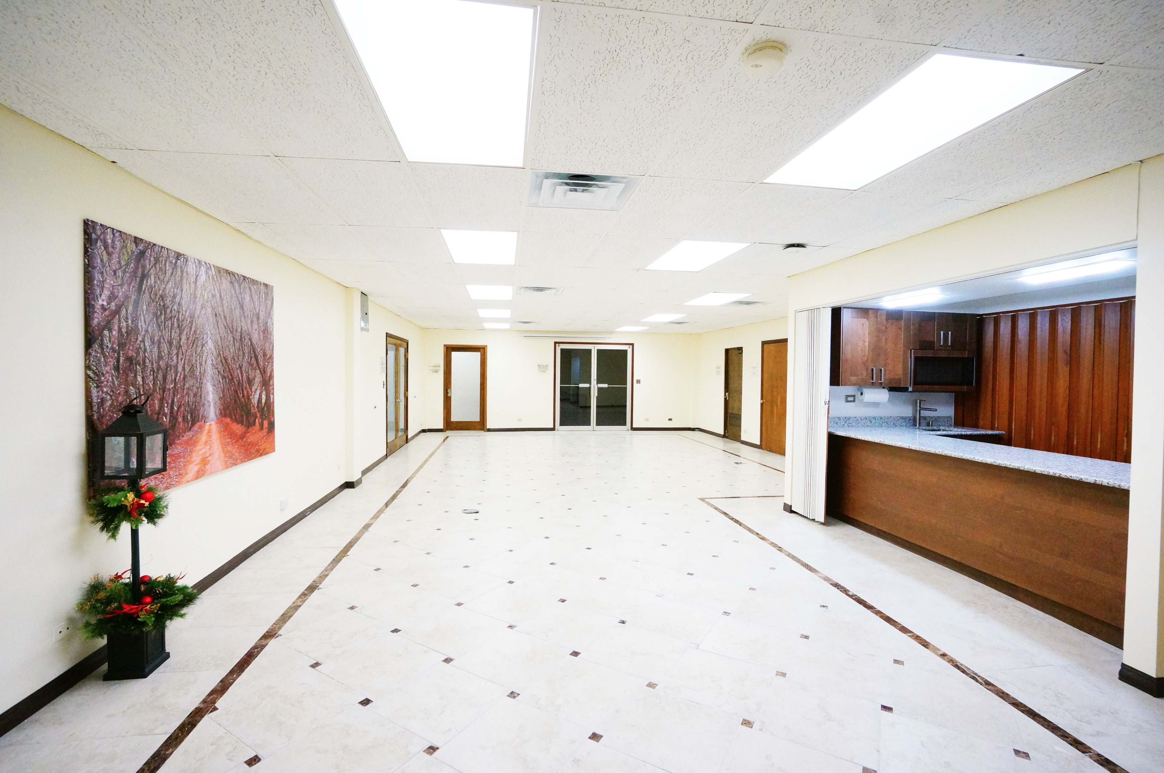 The image shows a spacious, empty room with tiled flooring, a large wall mural of a pathway, and an open kitchen area in the background.