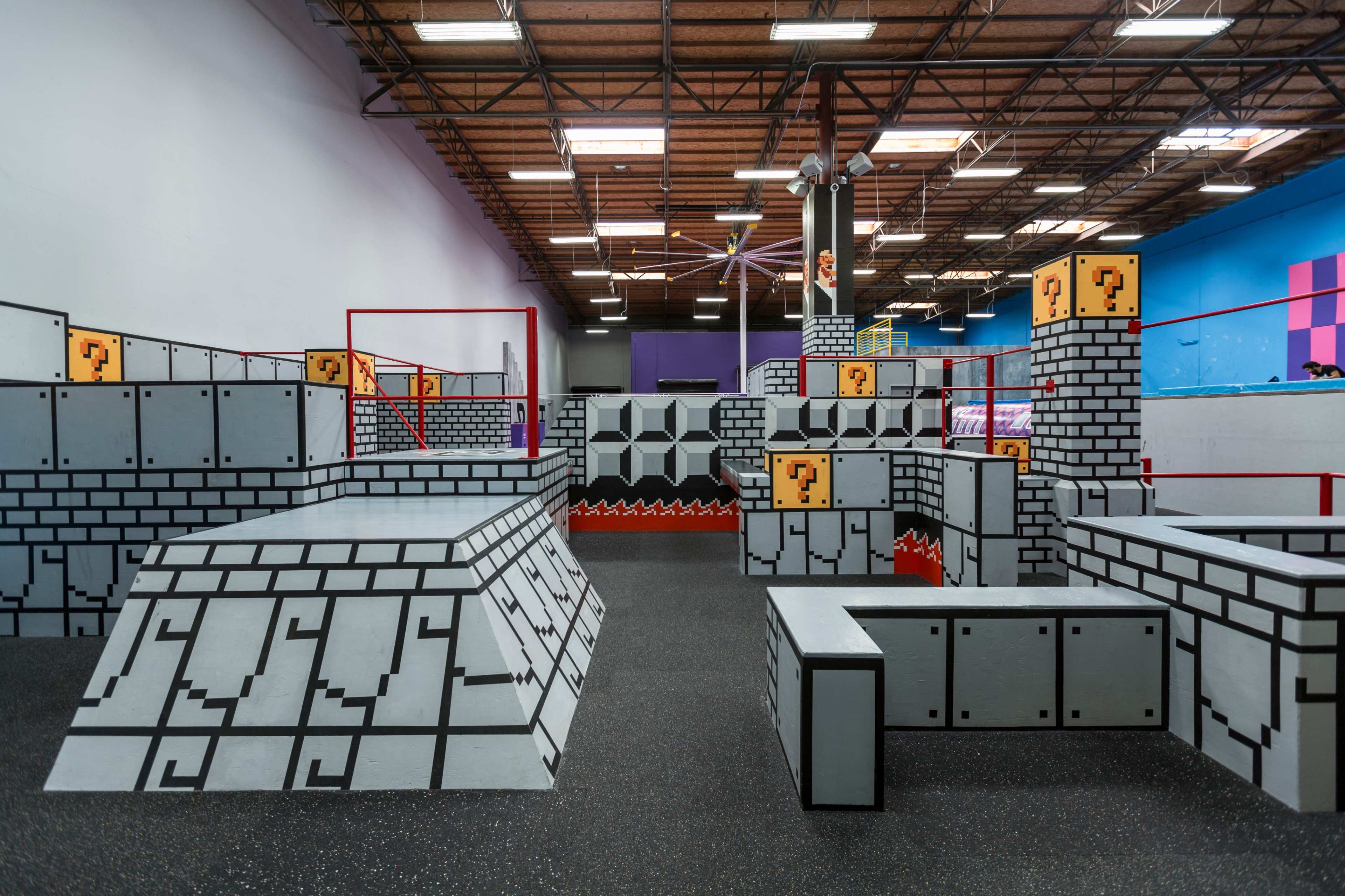An indoor play area designed to resemble a video game world, featuring obstacles like blocky structures, ramps, and a grid pattern on the floor.