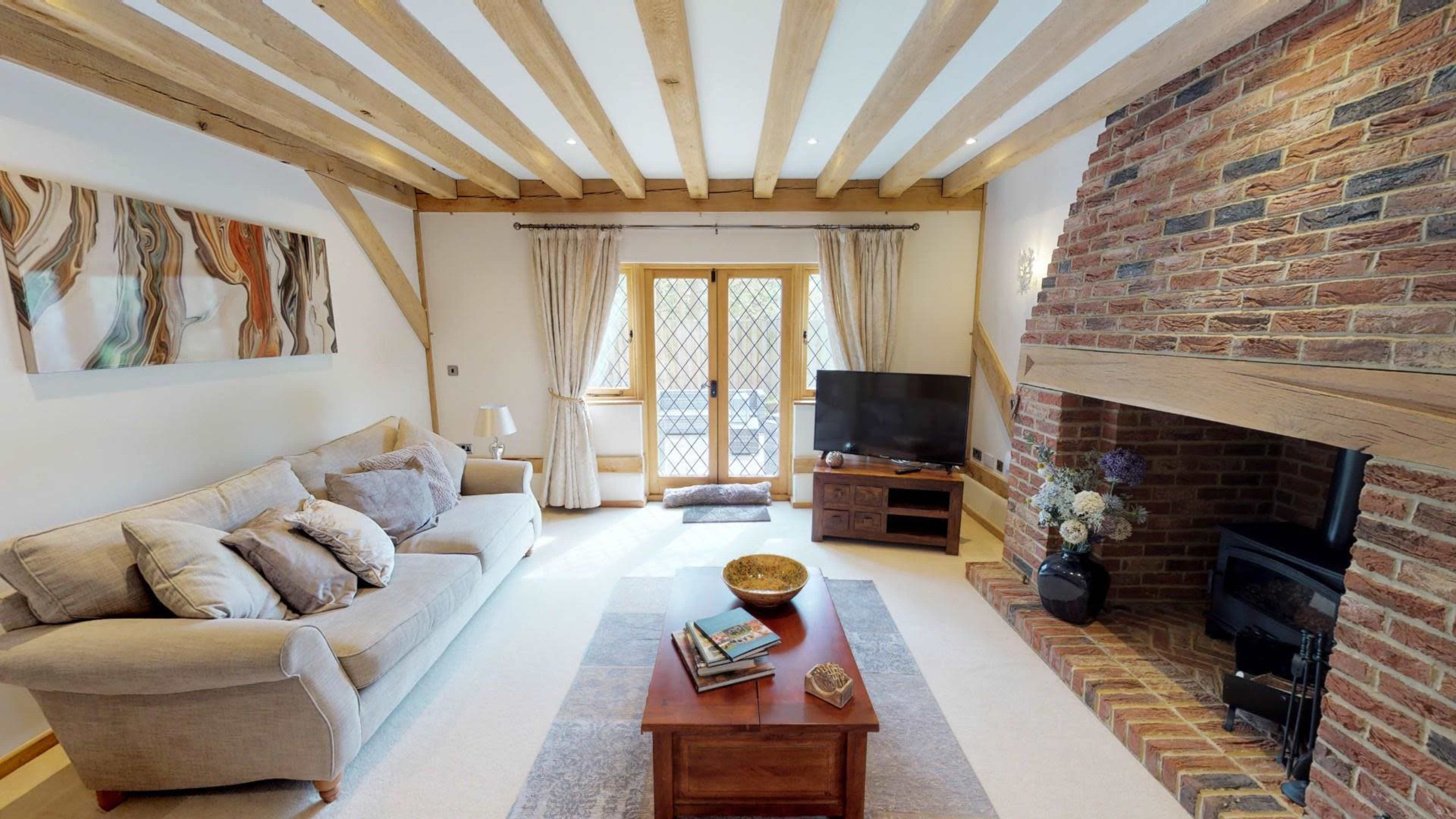A cozy living room features wooden beams, a brick fireplace, a television, and a sofa with a coffee table in front.