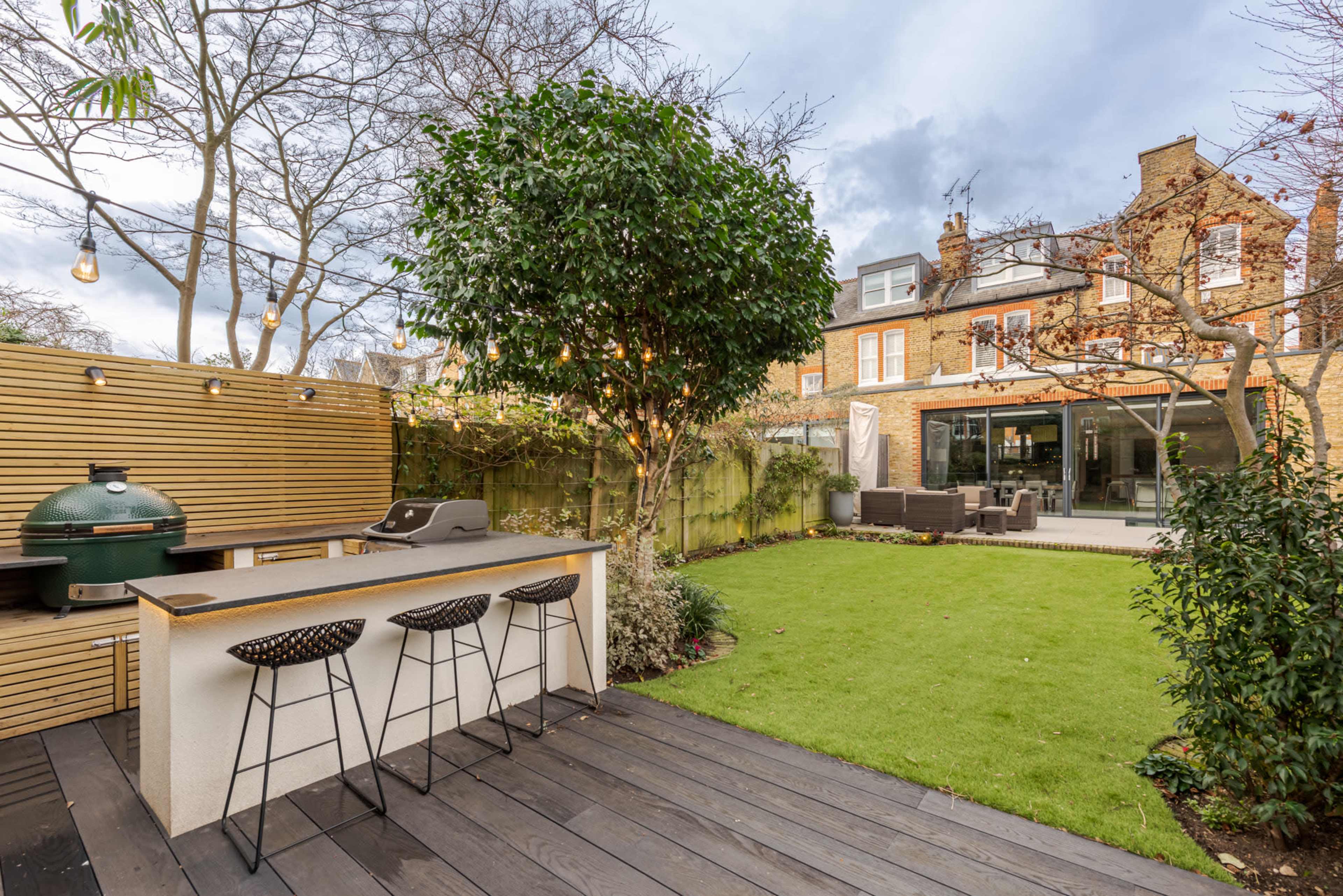 A landscaped backyard featuring a green lawn, a modern outdoor kitchen with seating, and a contemporary home in the background.