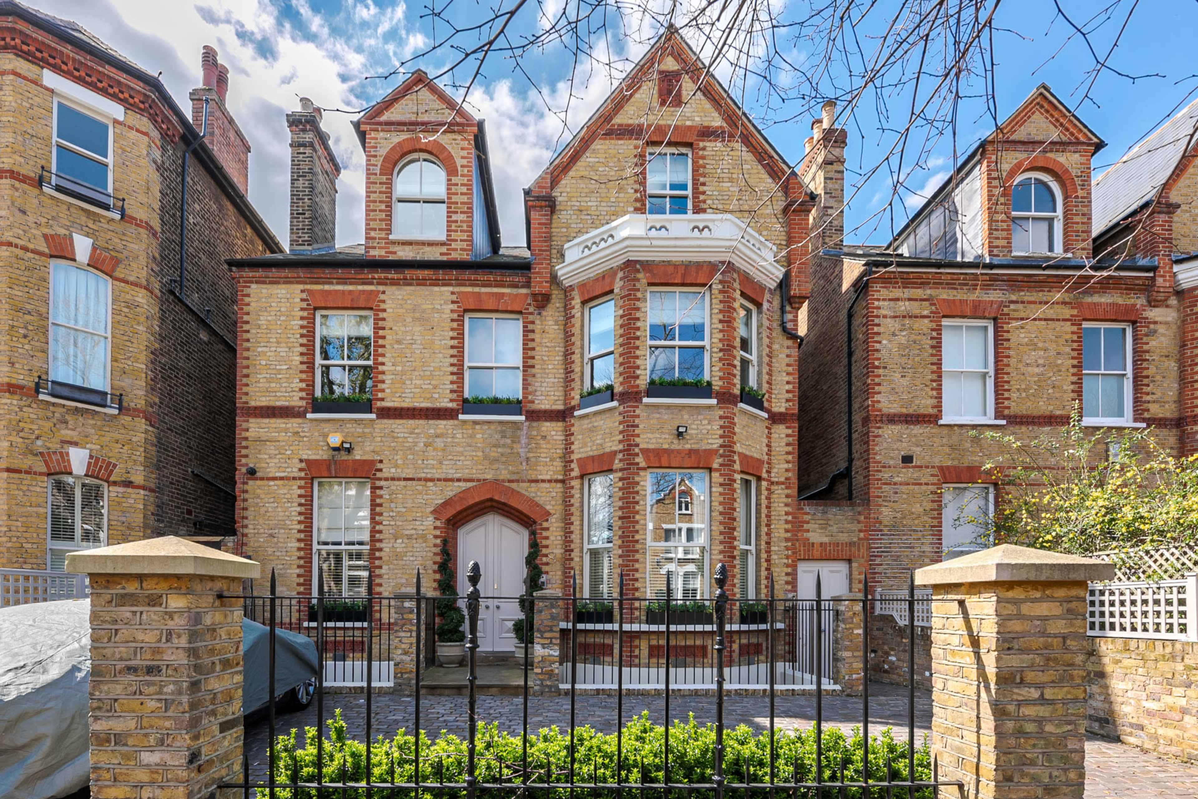 A three-story brick house with arched windows and a white doorway is flanked by two similar structures, enclosed by a low fence and greenery.