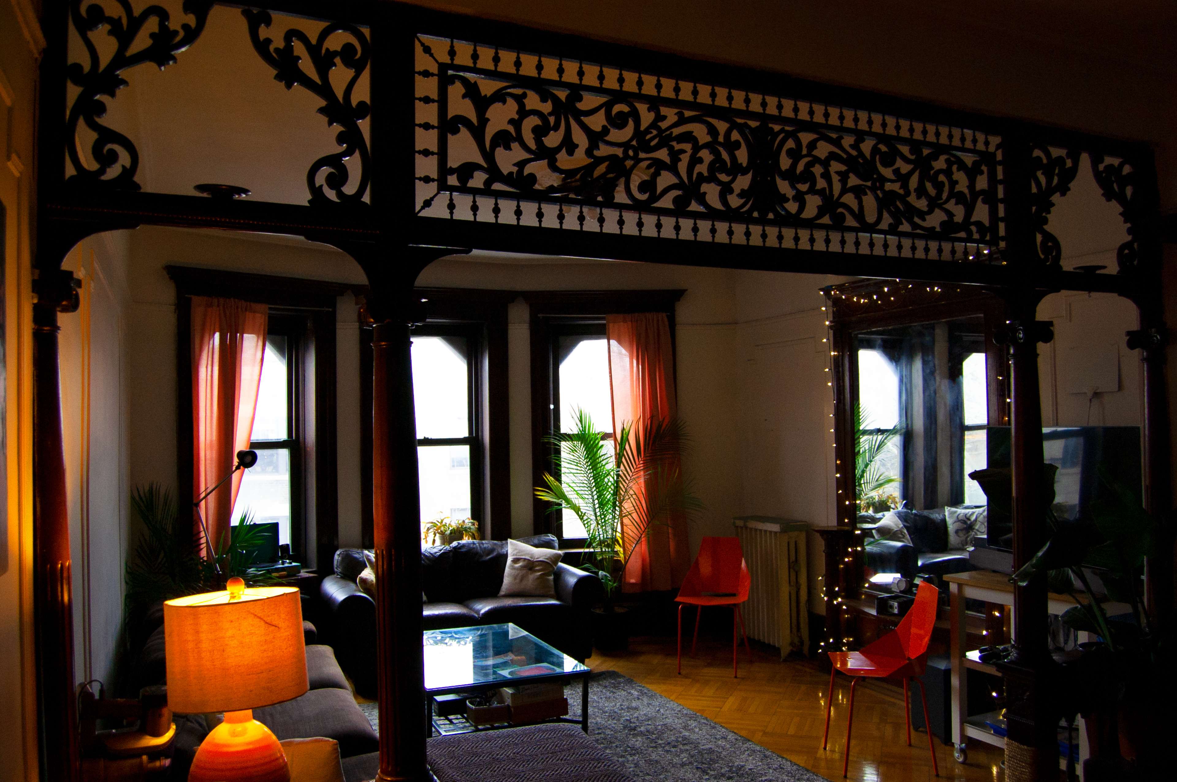 A cozy living room features large windows, a dark sofa, an ornate wooden archway, and decorative plants.