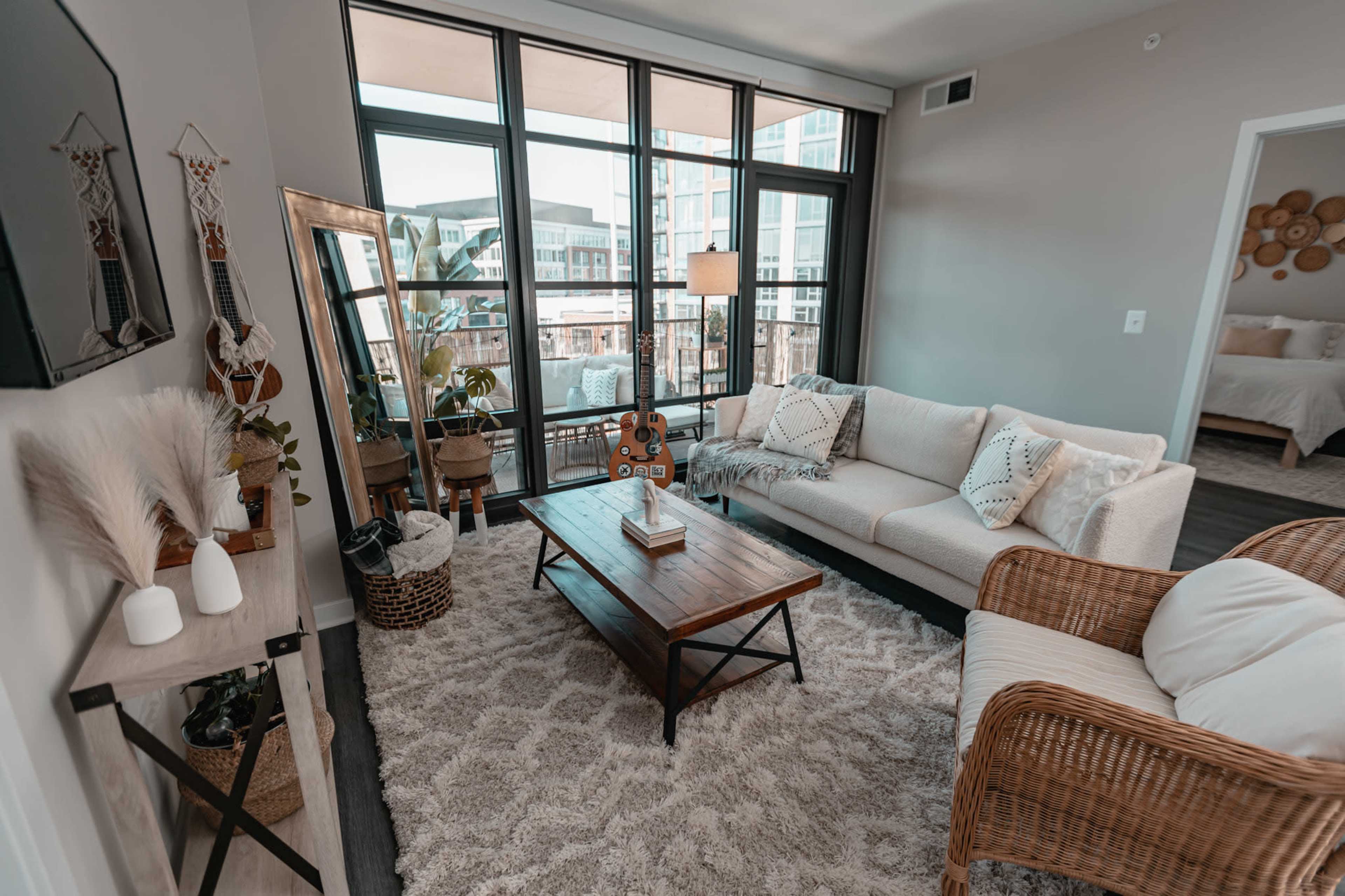 A modern living room features a light-colored sofa, a wooden coffee table, and large windows with a view of an urban landscape.