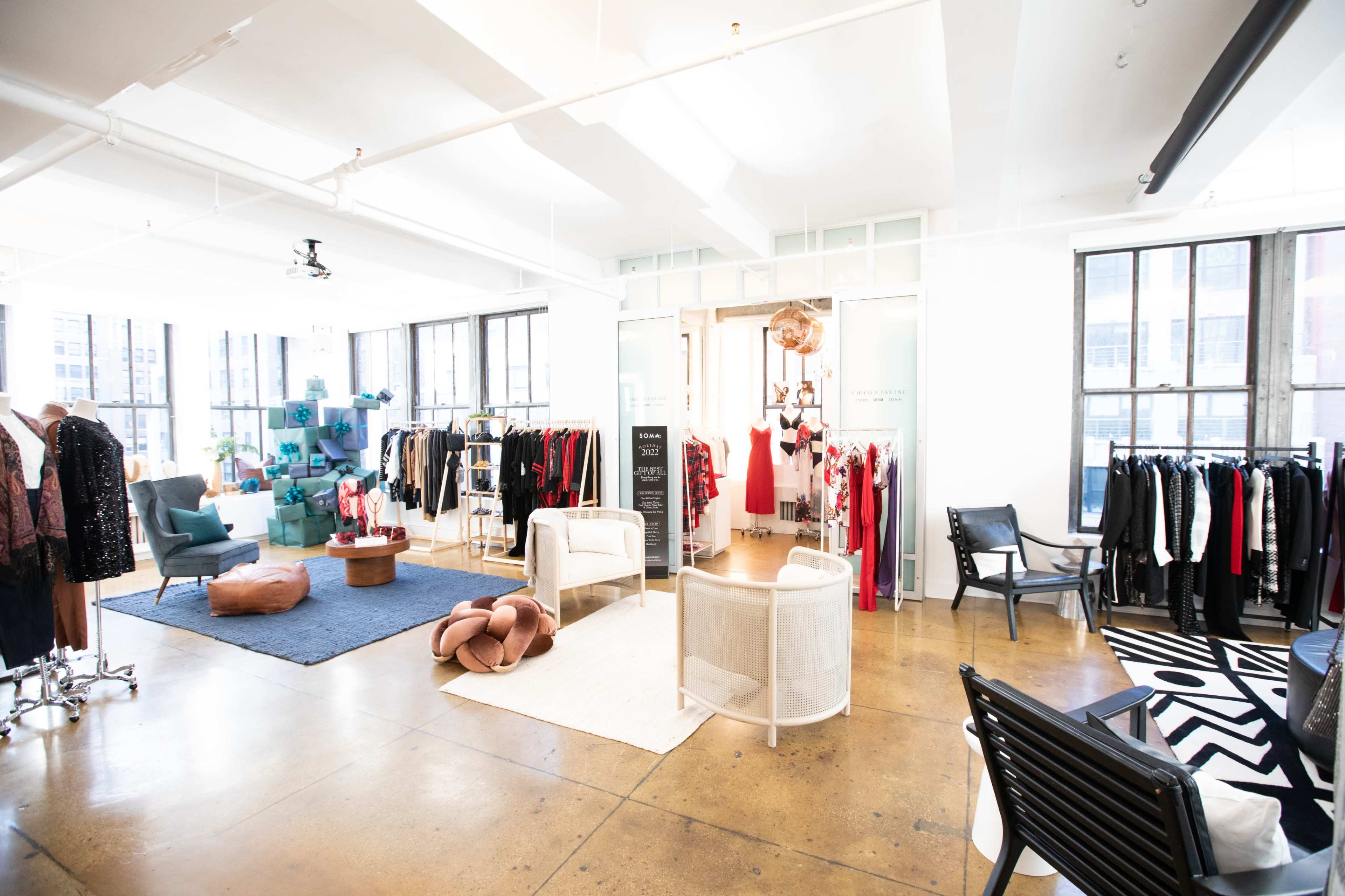 The image shows a modern clothing boutique featuring racks of apparel, various seating areas, and large windows allowing natural light.