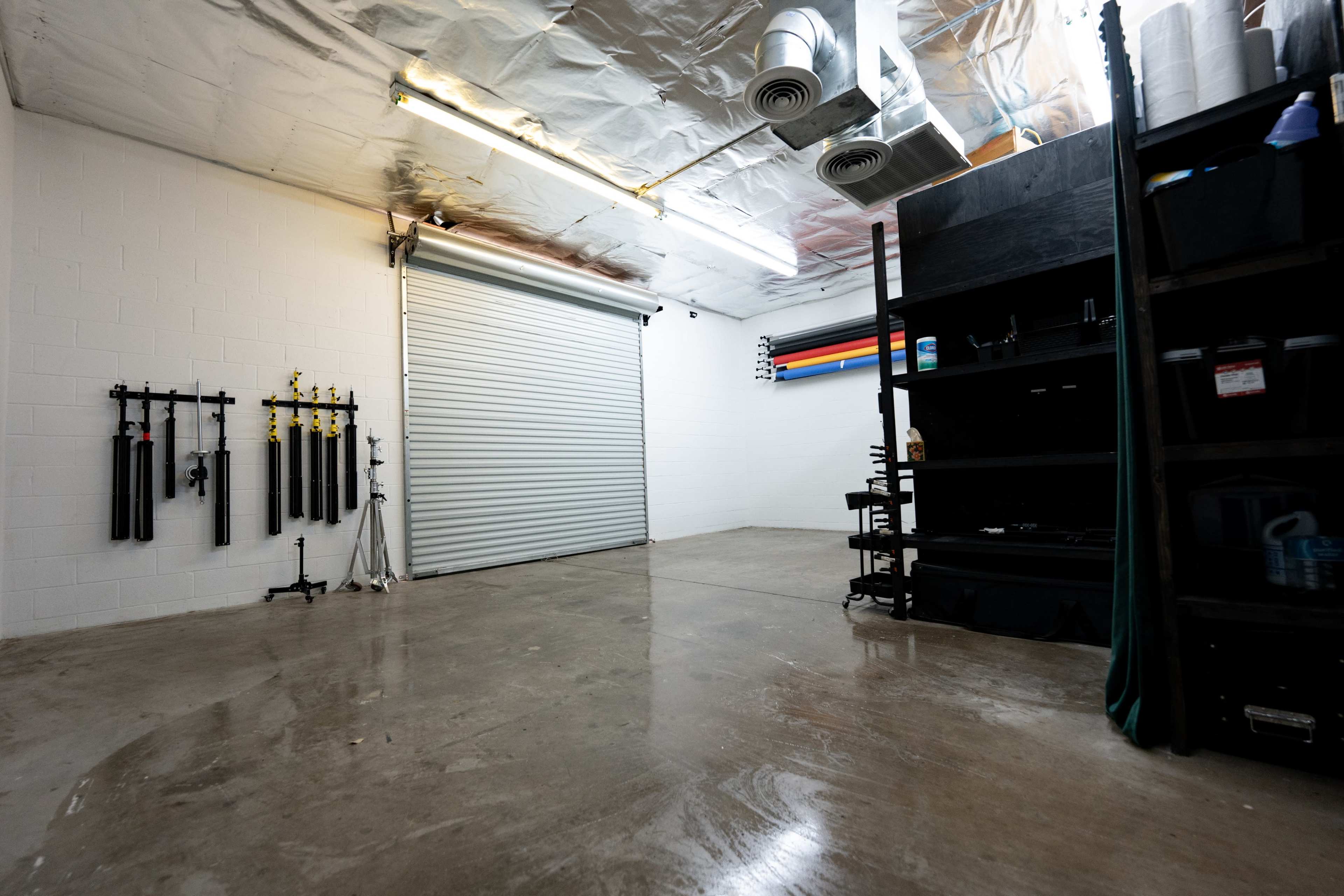 A spacious, clean garage or workshop with a sectional roll-up door, concrete floor, and equipment storage on one side.
