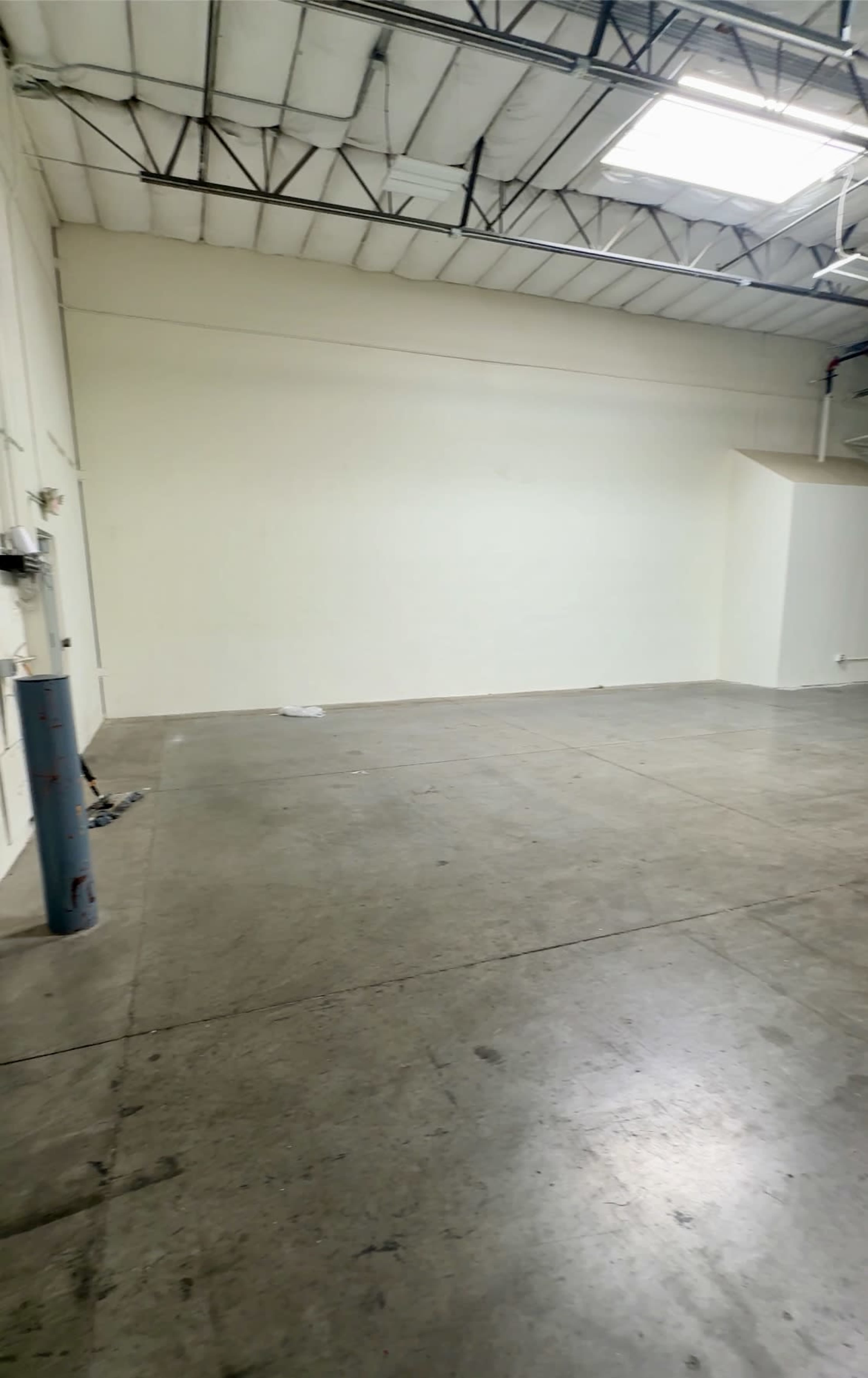 The image shows a spacious, empty industrial room with a concrete floor and white walls.