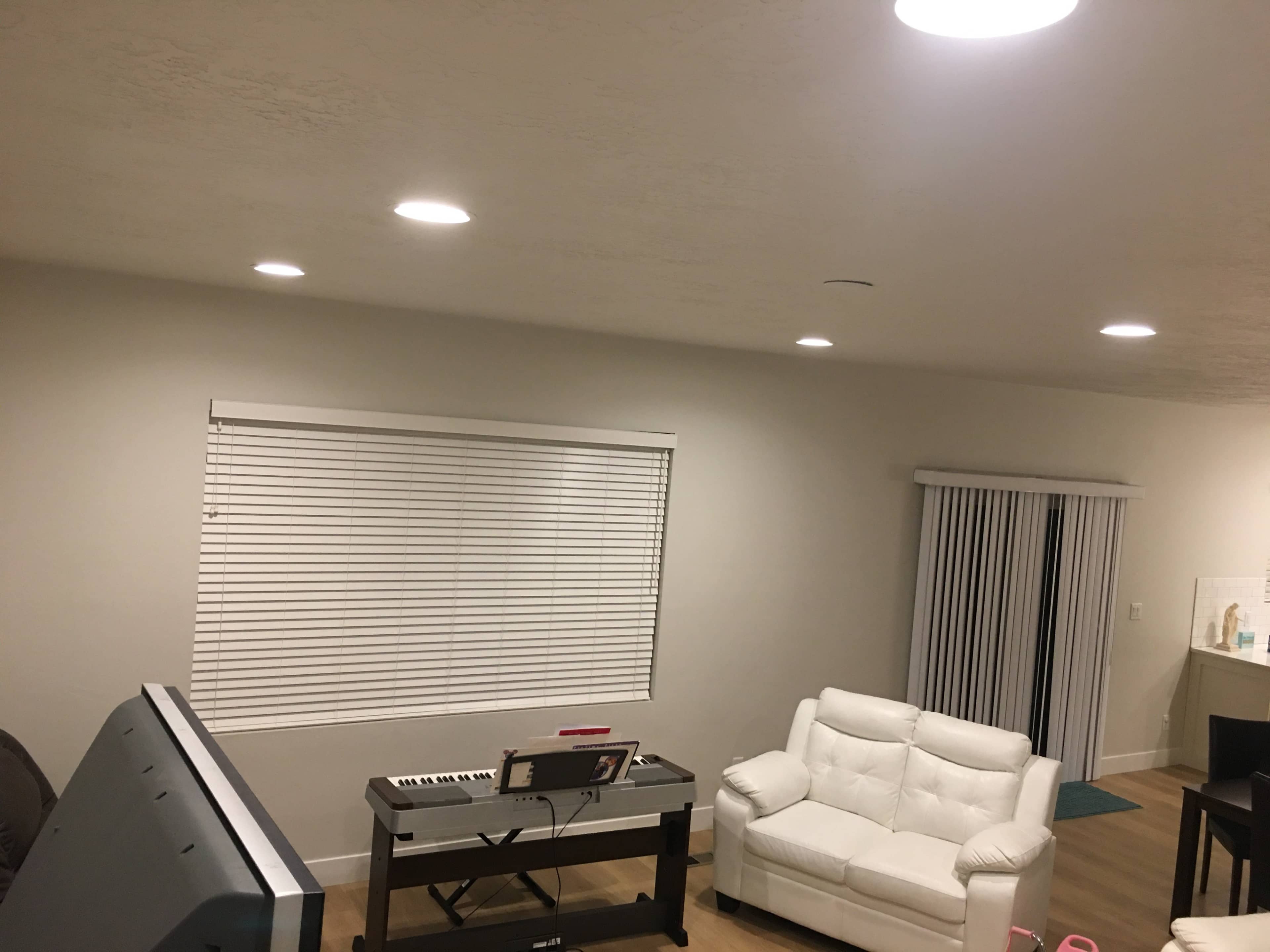 The image shows a living room with a white sofa, a keyboard on a table, a window covered with blinds, and sliding glass doors.