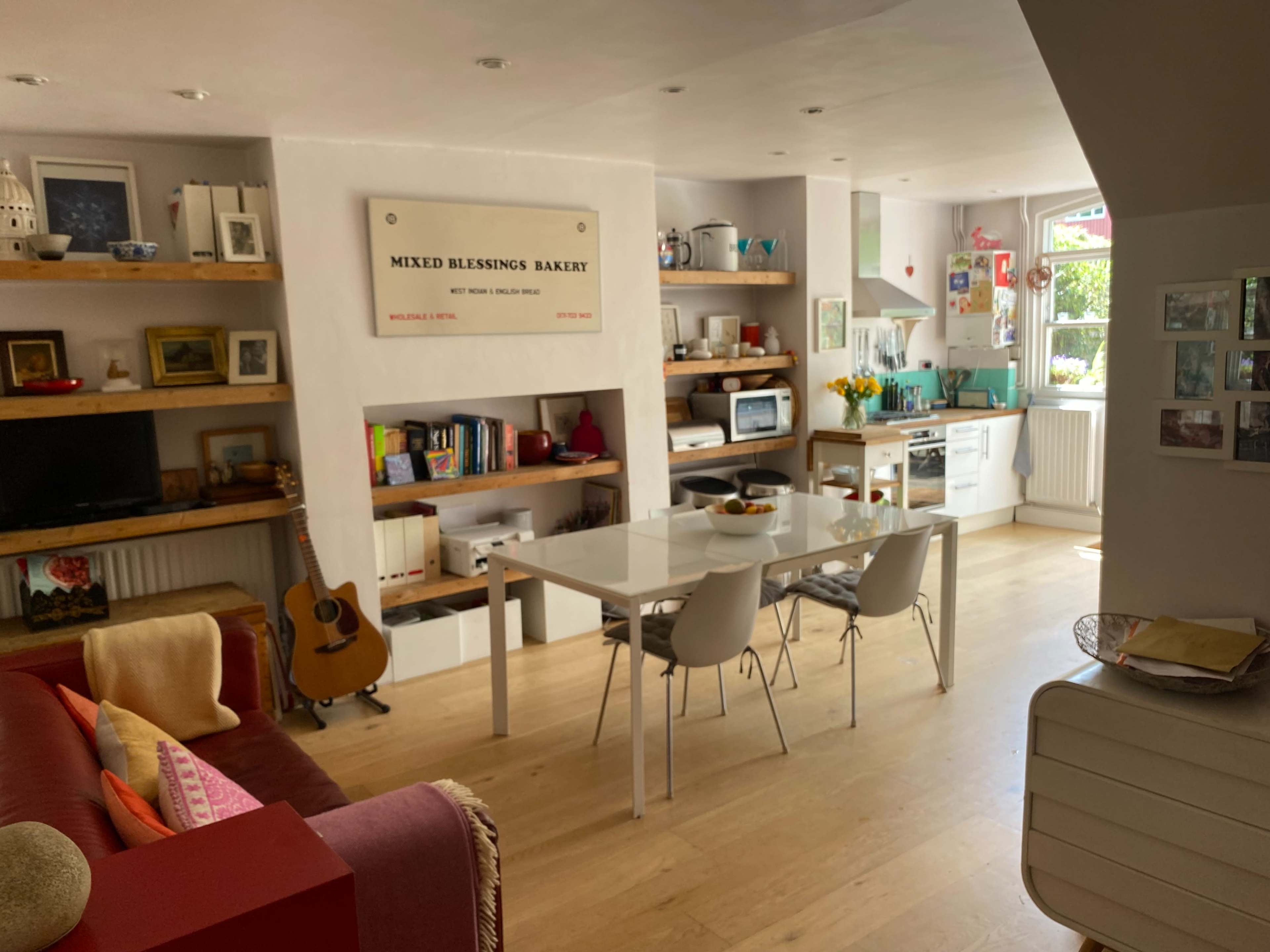 A bright and modern kitchen and dining area featuring a white table with chairs, wooden shelves with decorative items, and a guitar leaning against a wall.