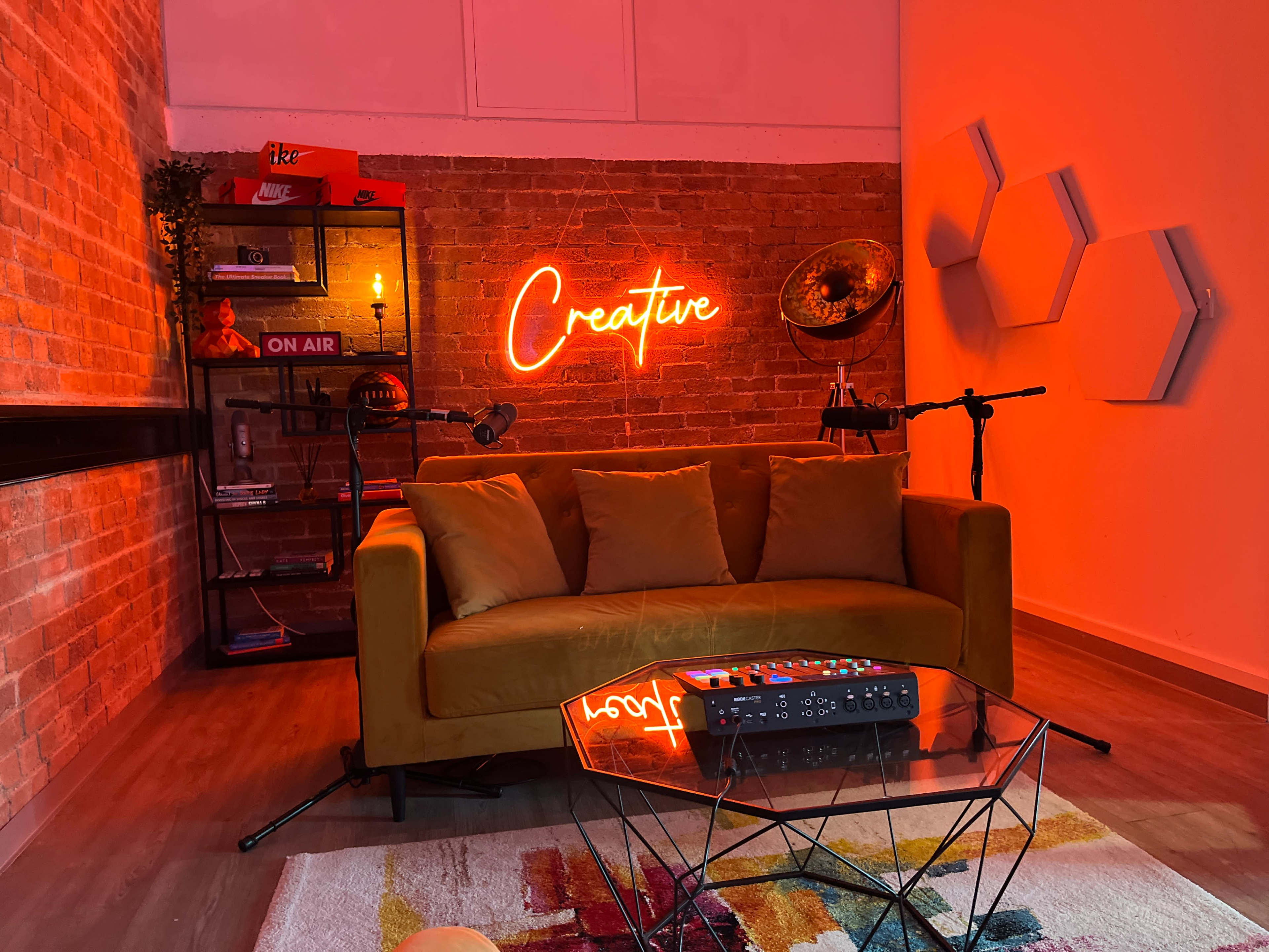 A cozy room with a yellow couch, a neon sign reading "Creative," and a small table in front of a brick wall adorned with shelves and decorative items.