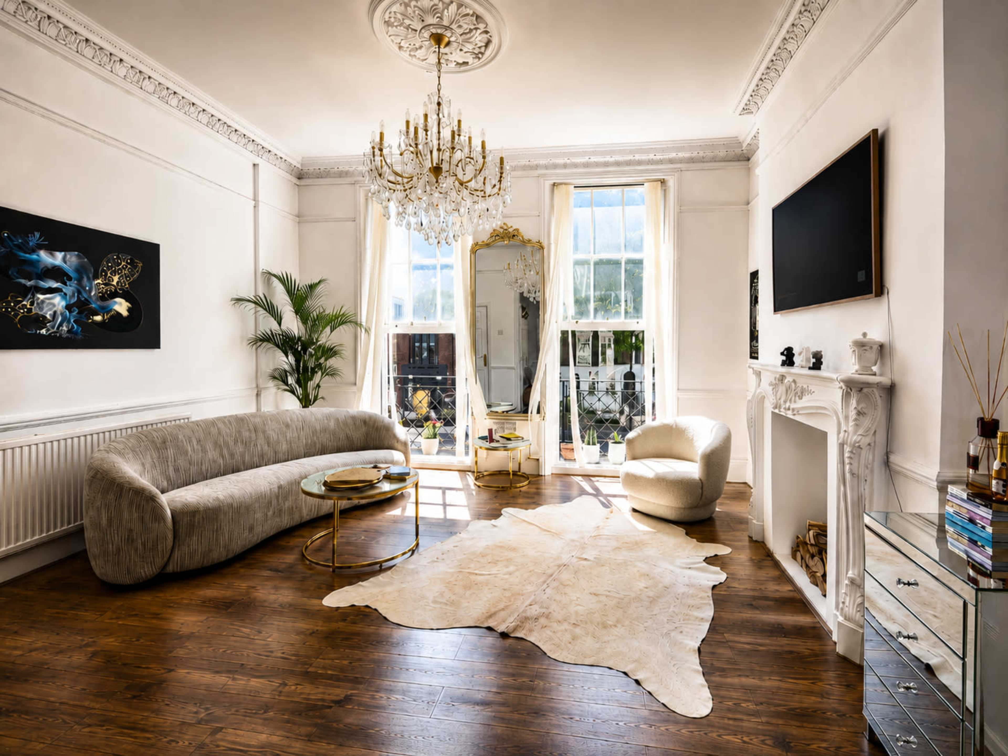 The image shows a stylish living room featuring a curved sofa, a chandelier, and large windows that allow natural light to illuminate the space.