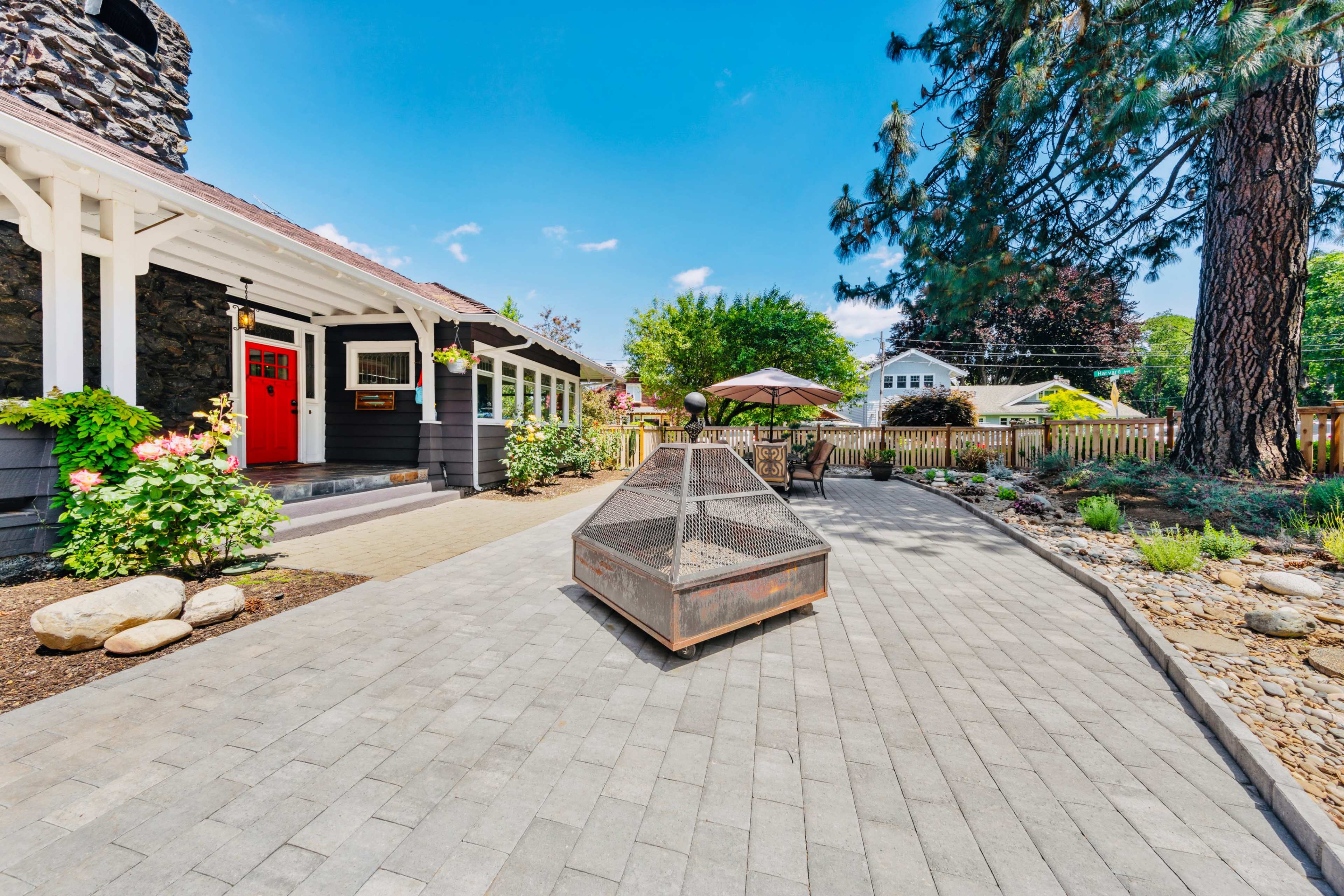 A stone house with a bright red door is surrounded by a paved patio and landscaped garden, featuring a fire pit and outdoor seating area.