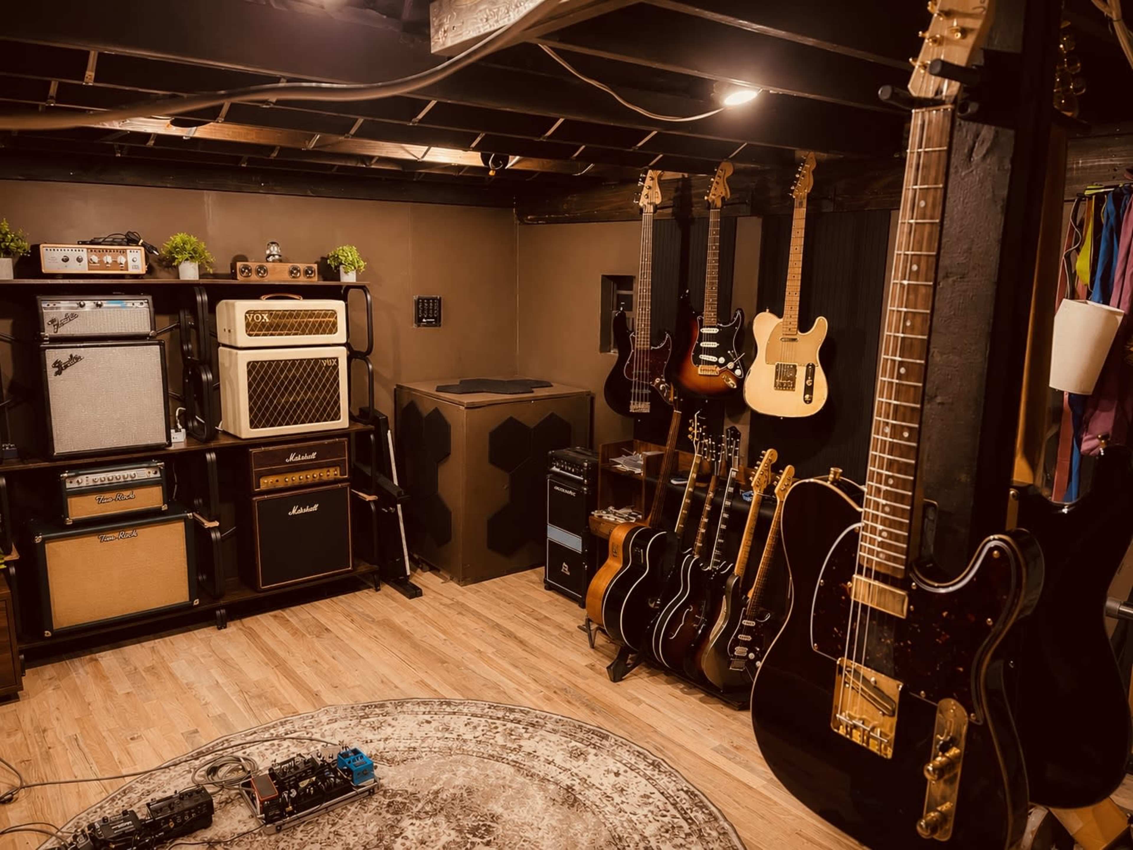 The image shows a music room with various electric guitars, amplifiers, and a round rug on a wooden floor.