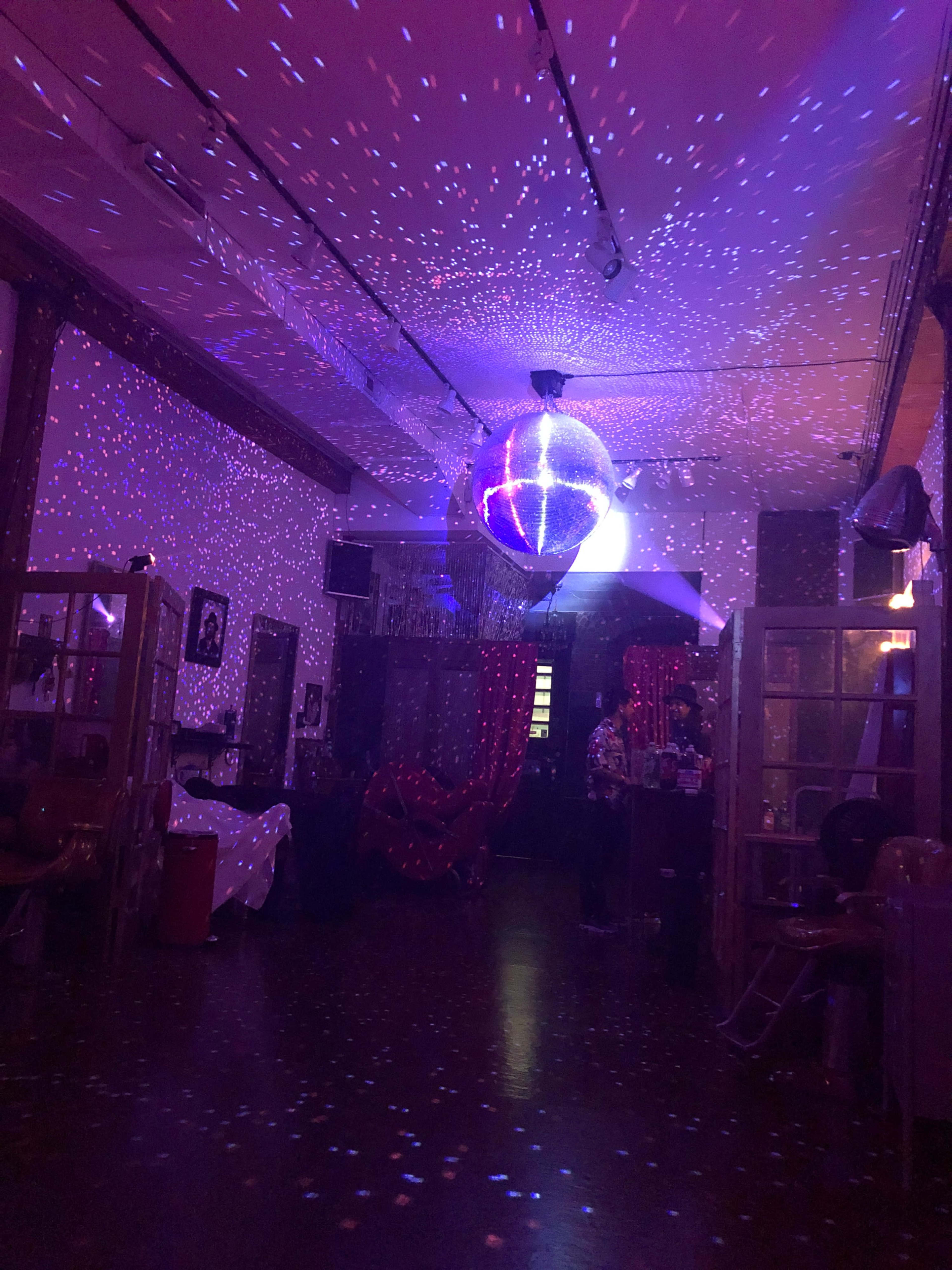 The image shows a dimly lit room with colorful lights projected onto the walls and floor, featuring a large disco ball hanging from the ceiling.