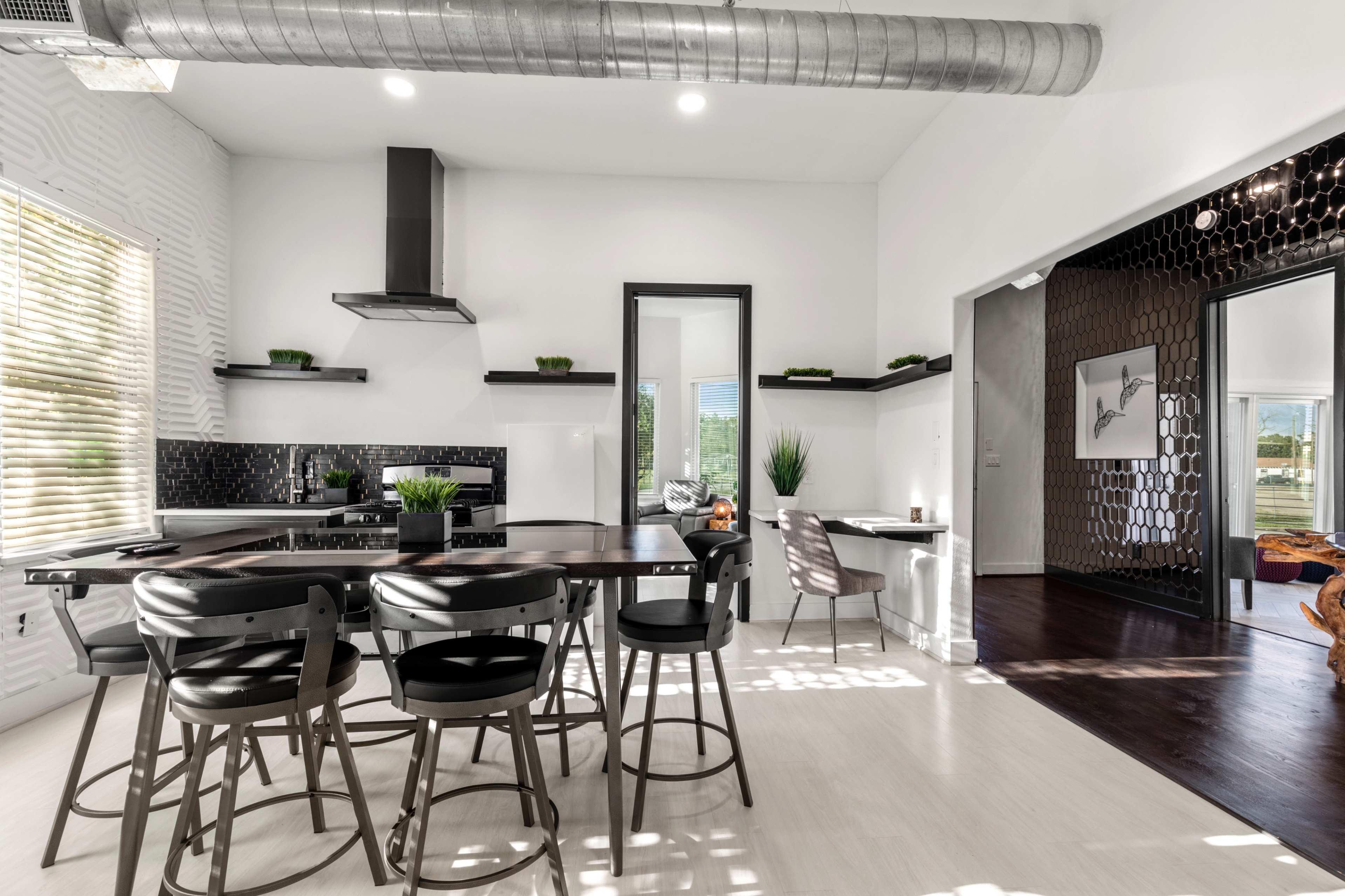 A modern kitchen with a dining area featuring black and white decor, stainless steel appliances, and a large window providing natural light.