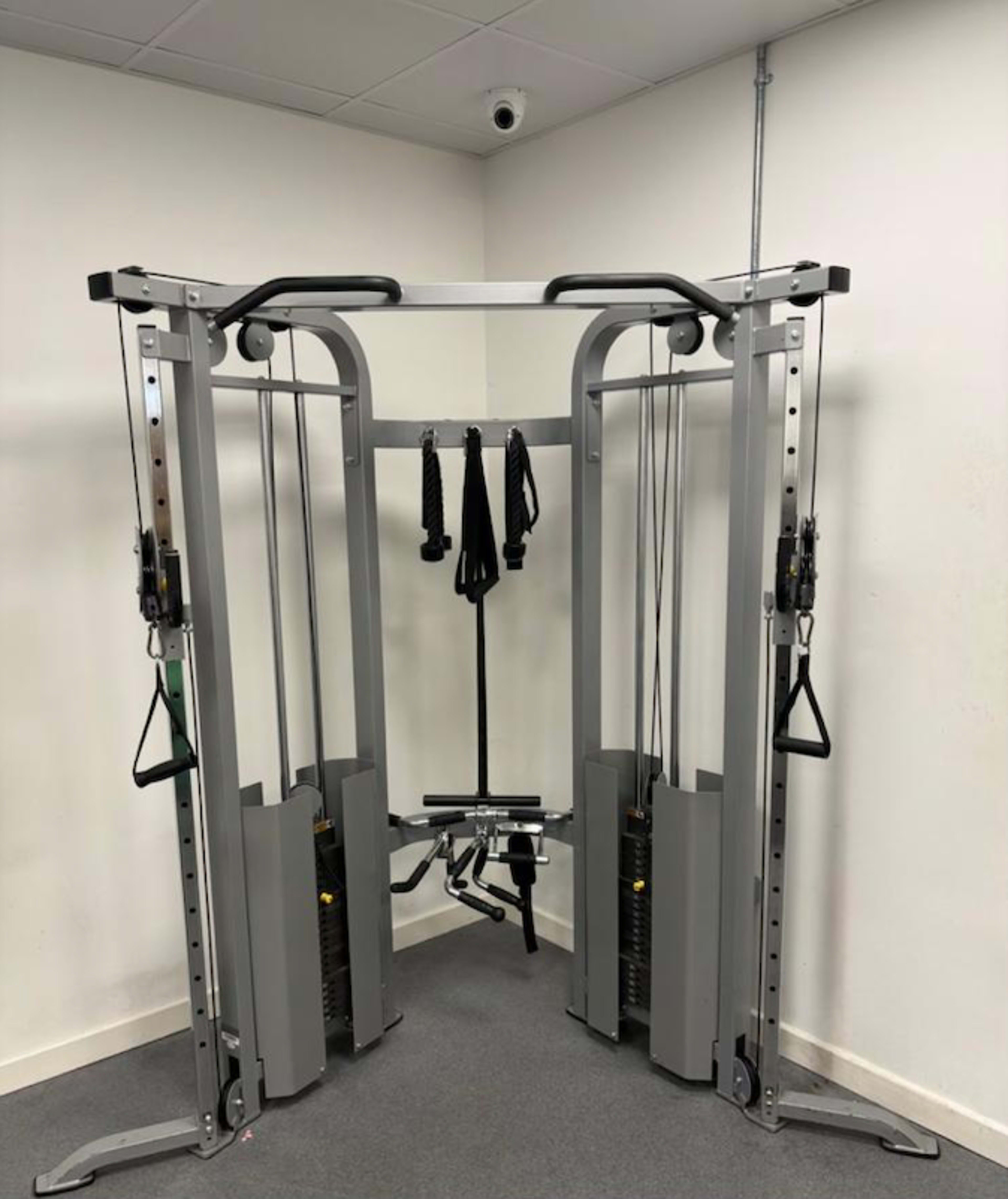 The image shows a multi-station gym workout machine with cables, pulleys, and adjustable weight stacks.