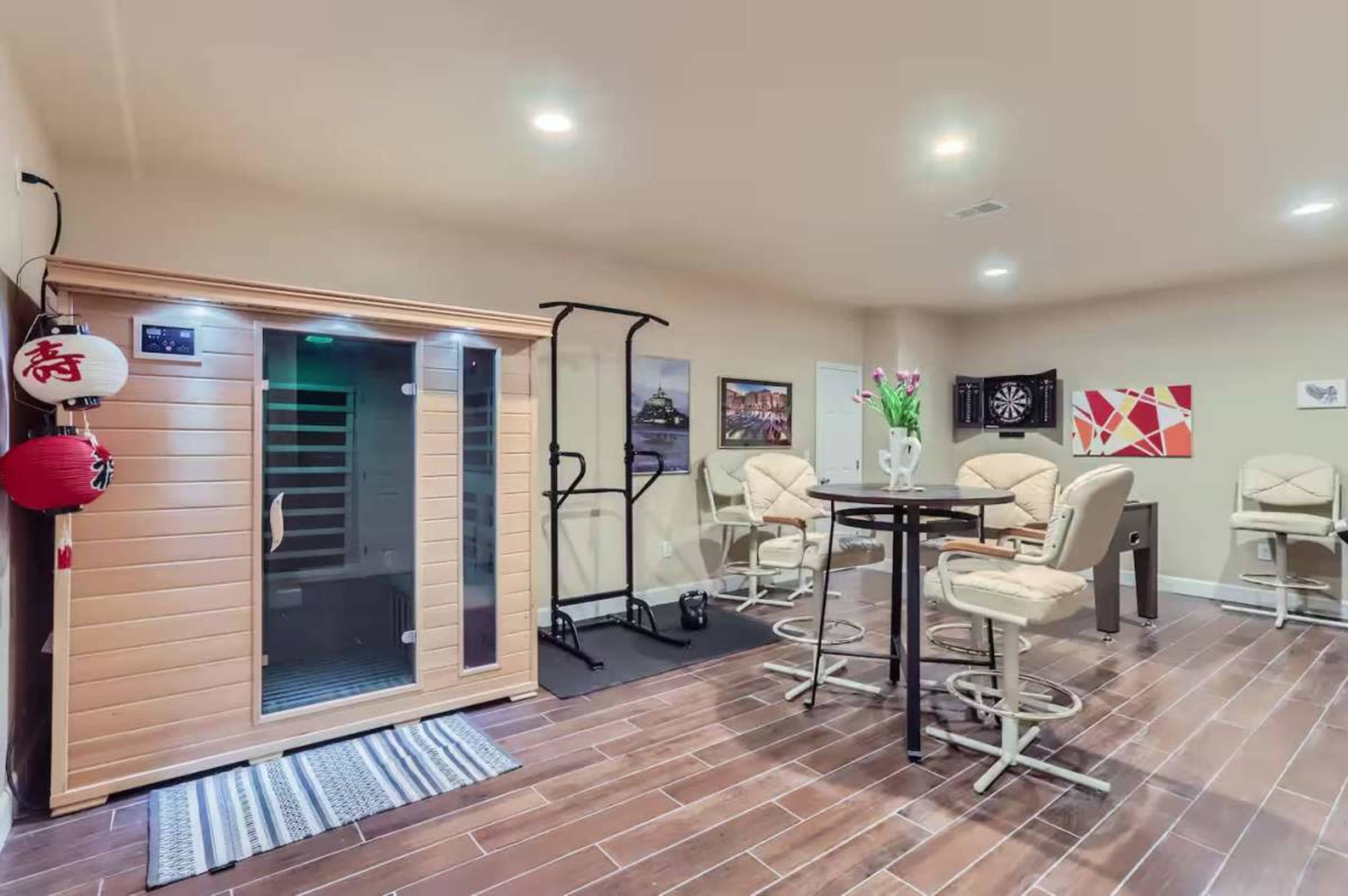 The image shows a home recreation room featuring a sauna, exercise equipment, and a bar area with high-top seating.