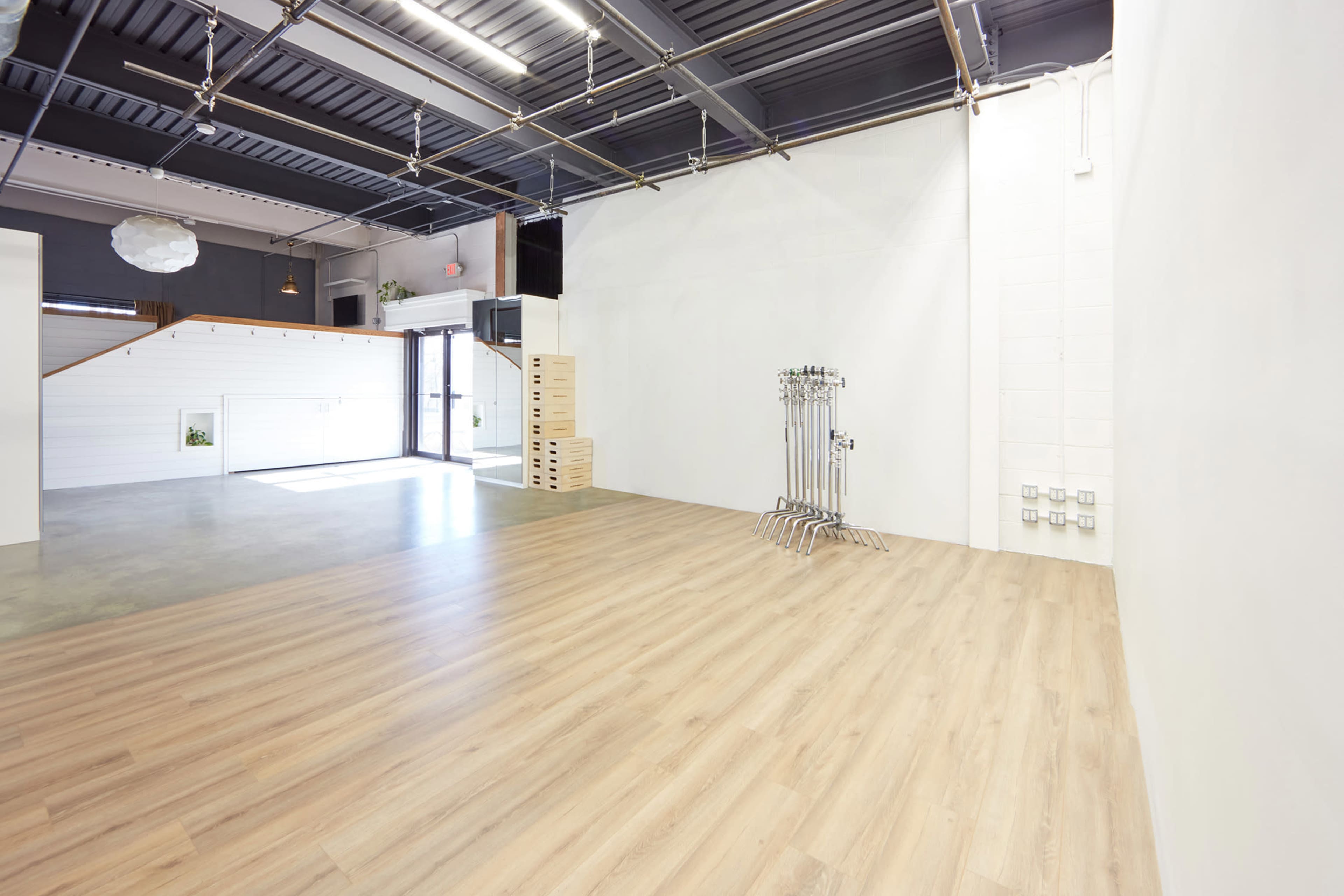 A spacious, empty interior with wooden flooring and white walls, featuring large windows and minimalist decor.