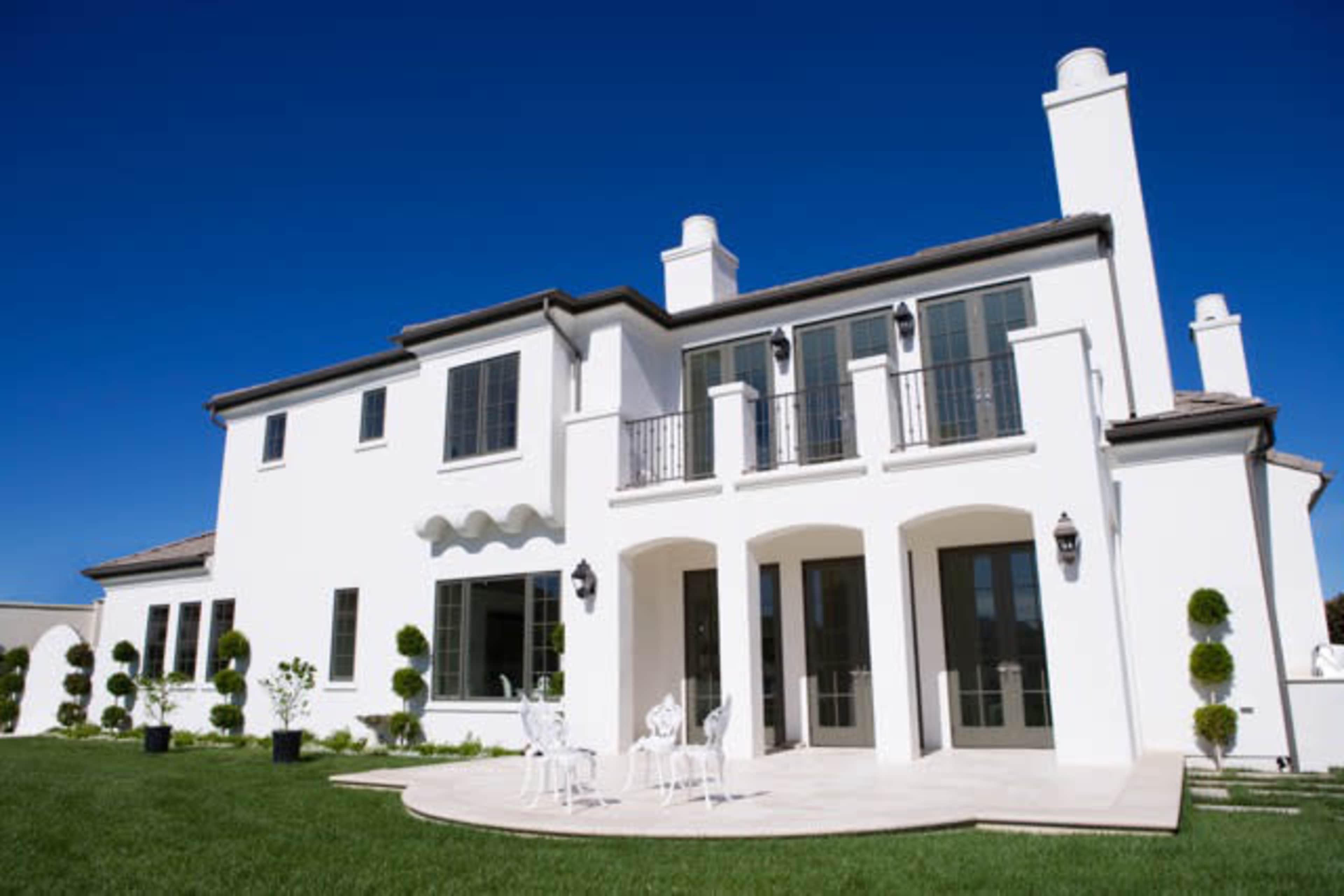 A modern, two-story white house features large windows, balconies, and a well-manicured lawn.