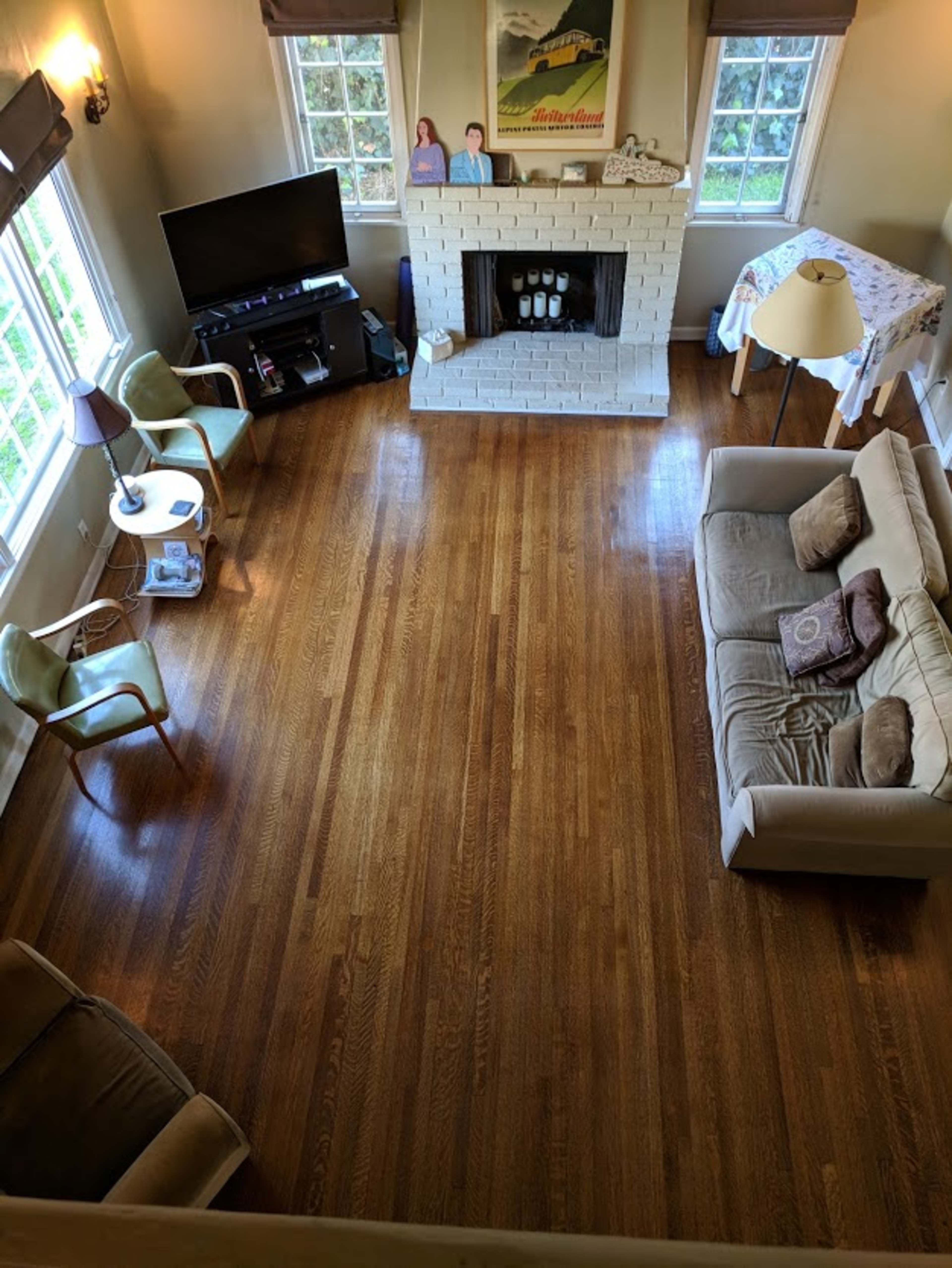 A living room with hardwood floors, a white brick fireplace, a television stand, two chairs, a lamp, and a couch.