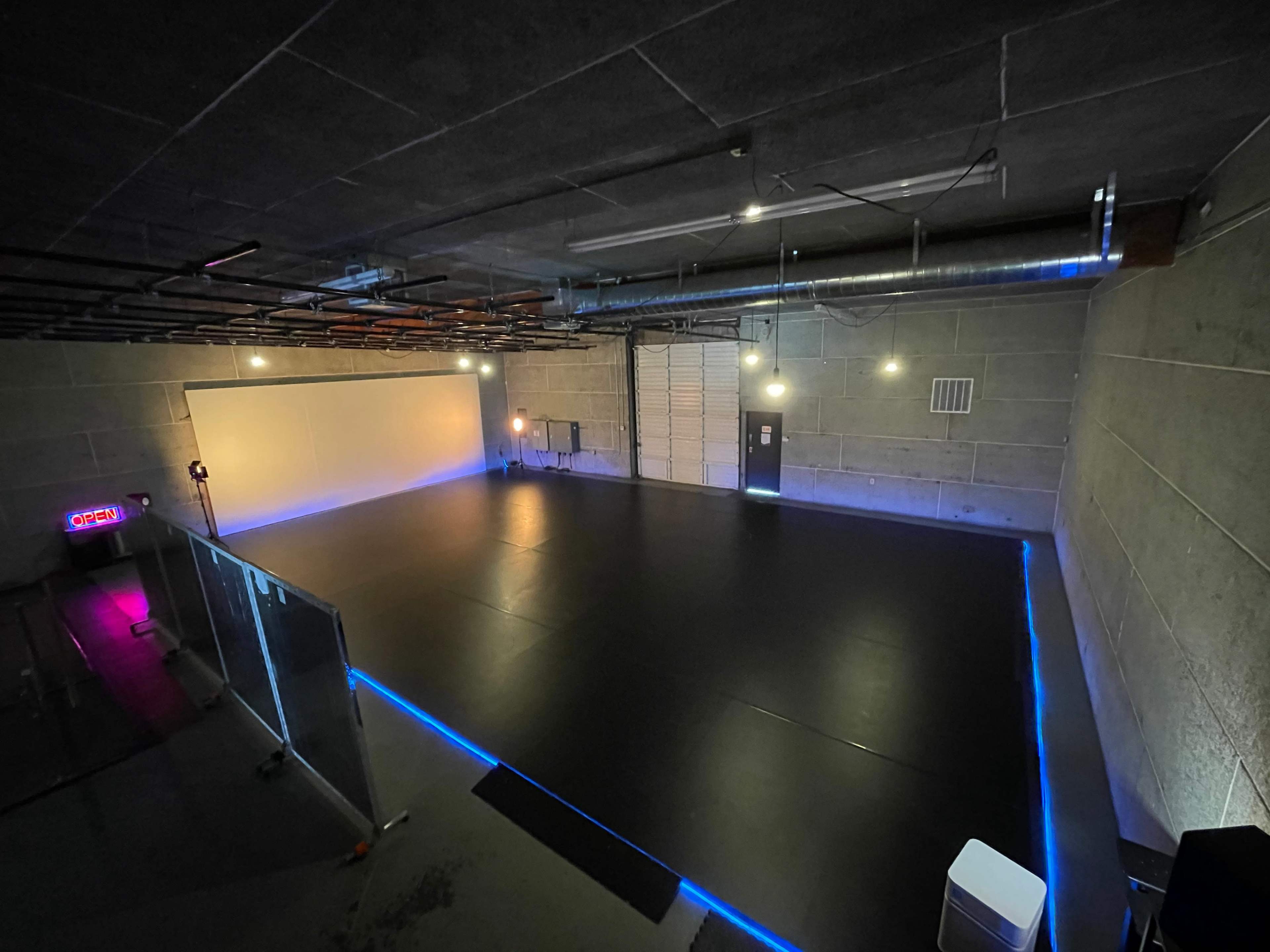 An empty room with a black floor and LED lighting along the edges, set against concrete walls.