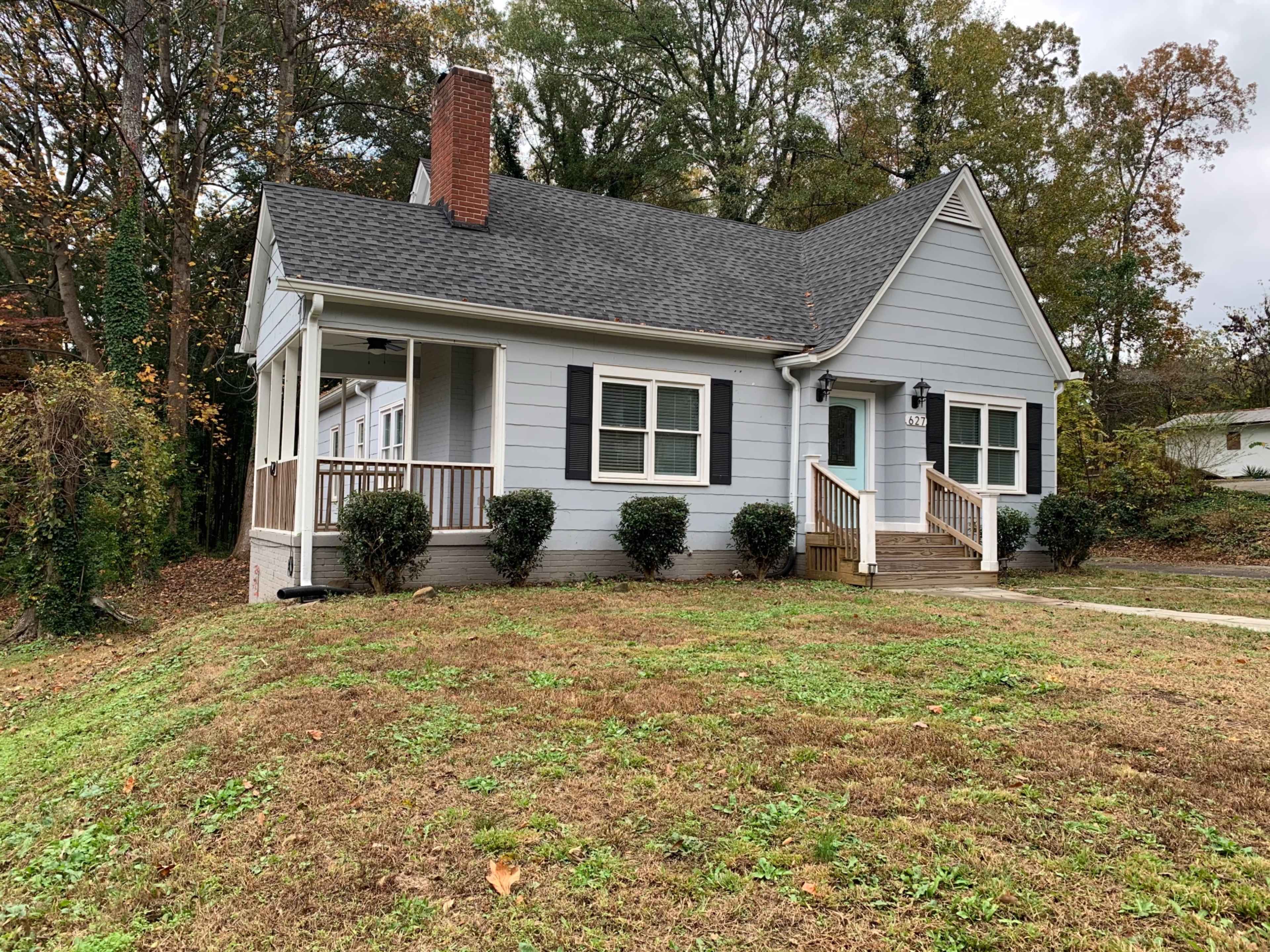 A single-story gray house with a front porch, white trim, and landscaped bushes in the yard.