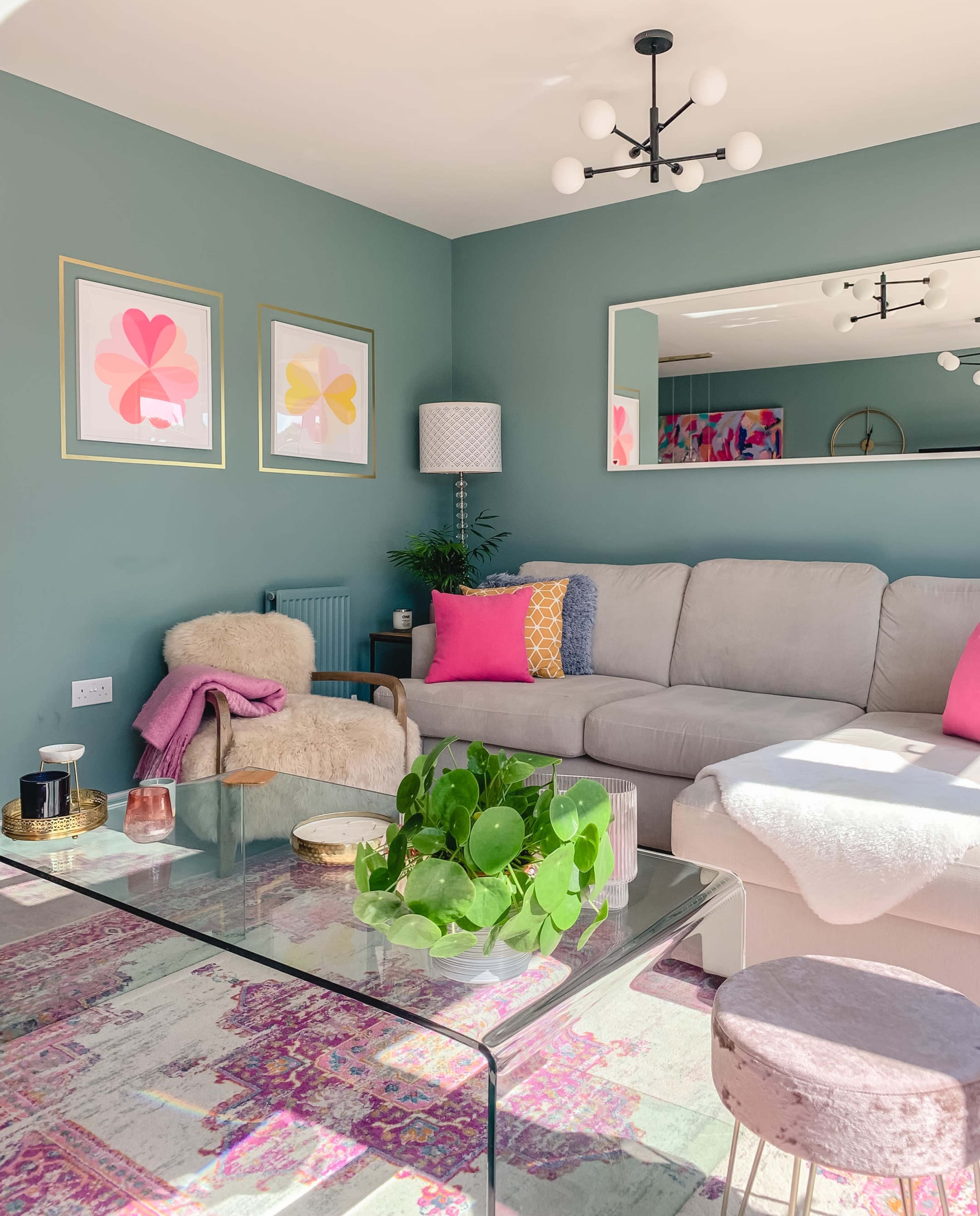 A bright and modern living room features a gray sectional sofa, colorful wall art, and a glass coffee table surrounded by decorative items.