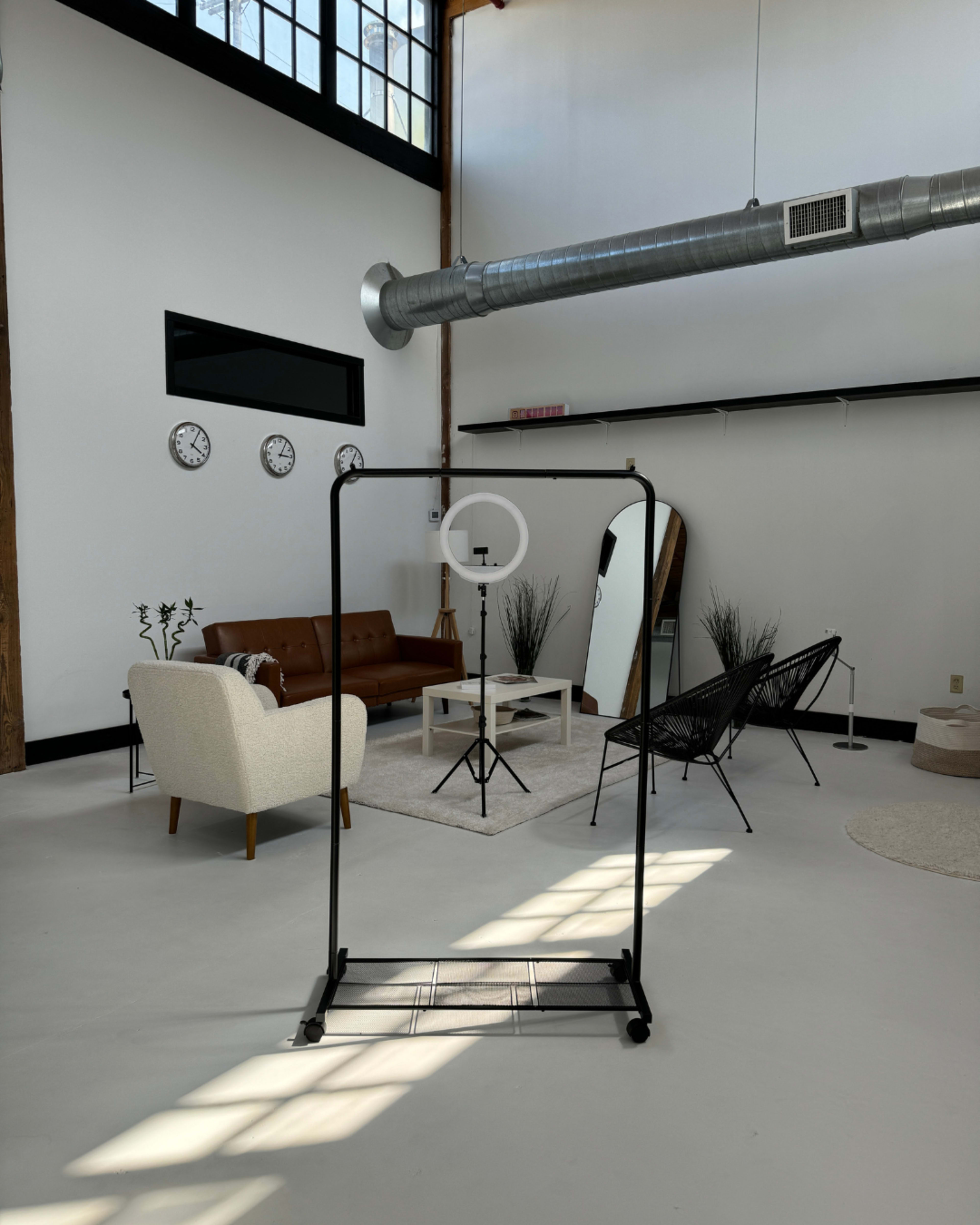 A spacious, modern interior with a seating area featuring a couch and chairs, a mirror on a clothing rack, and wall clocks.