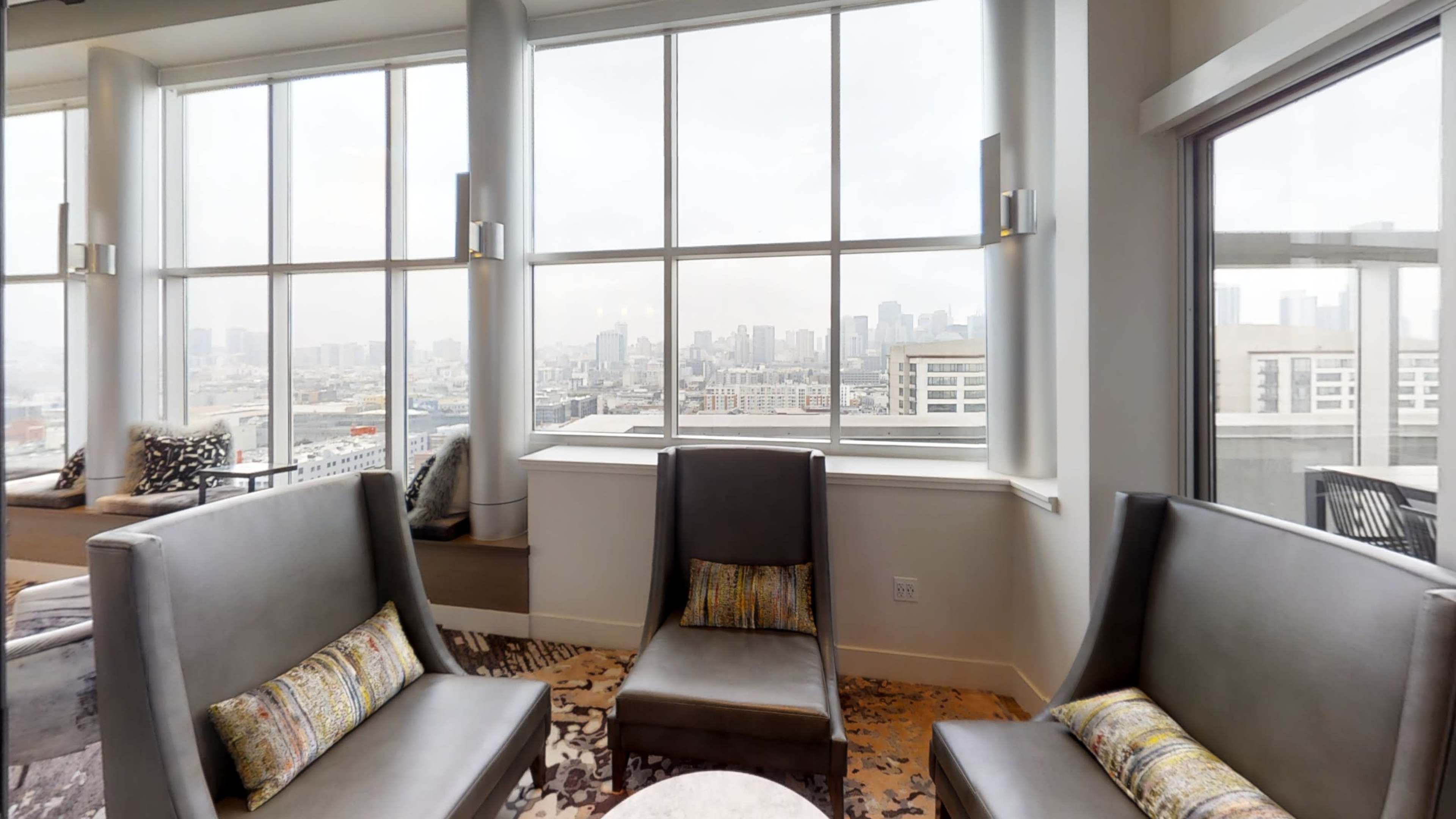 A modern lounge area with two gray chairs and a panoramic window displaying a city skyline.
