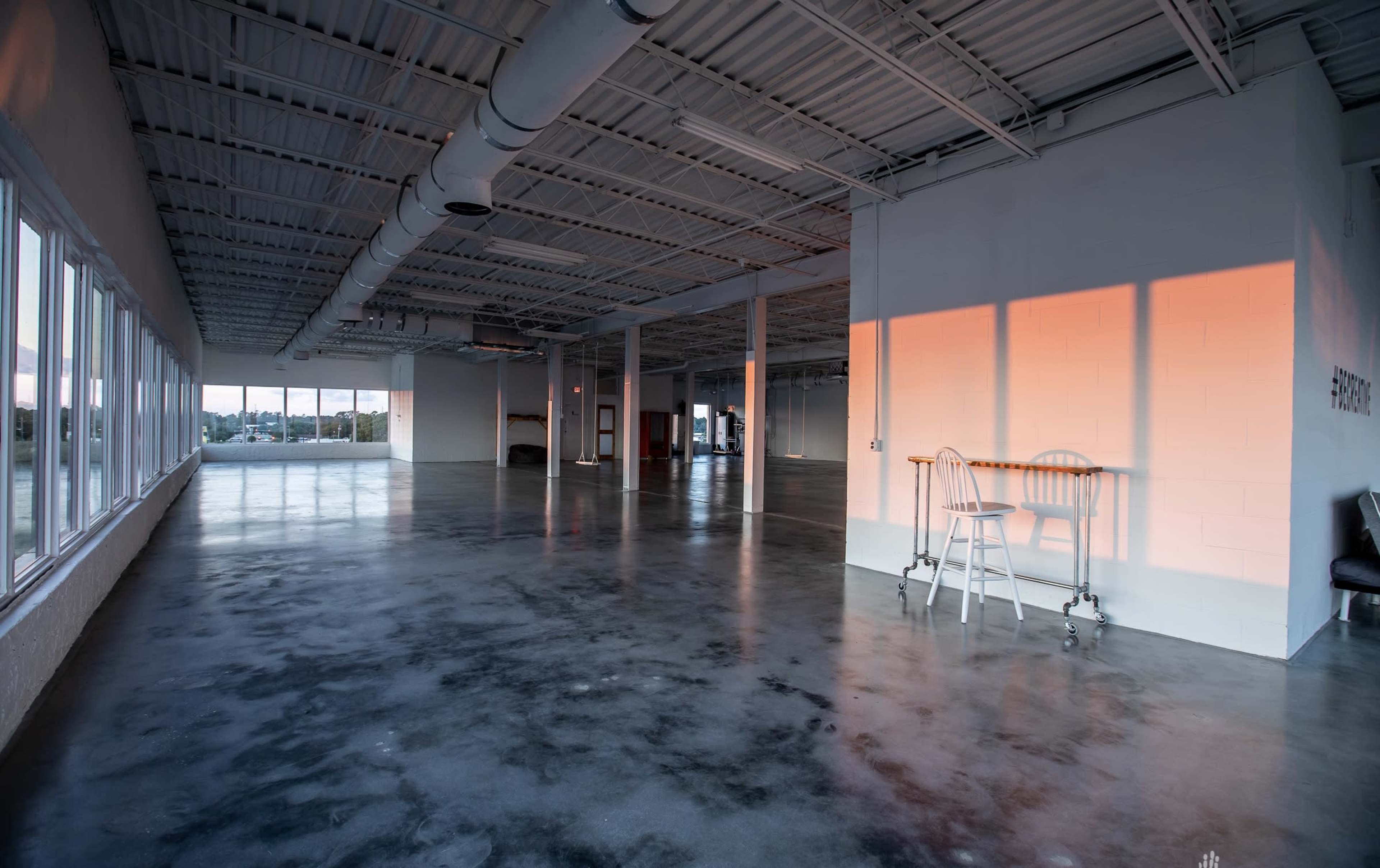 A spacious, empty room with polished concrete floors and large windows allowing natural light to illuminate the interior.
