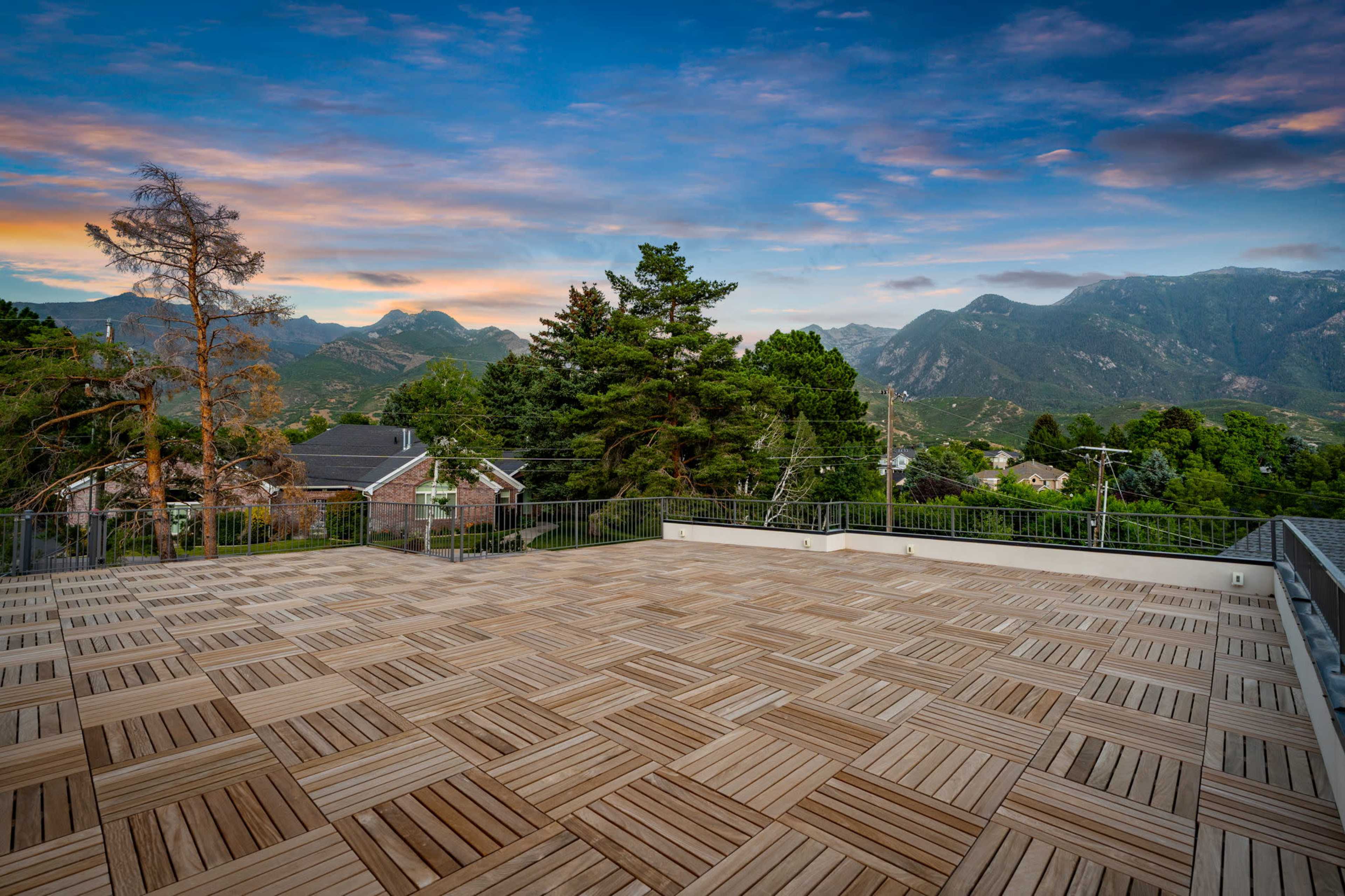 The image shows a wooden deck on a terrace overlooking a mountainous landscape during sunset.