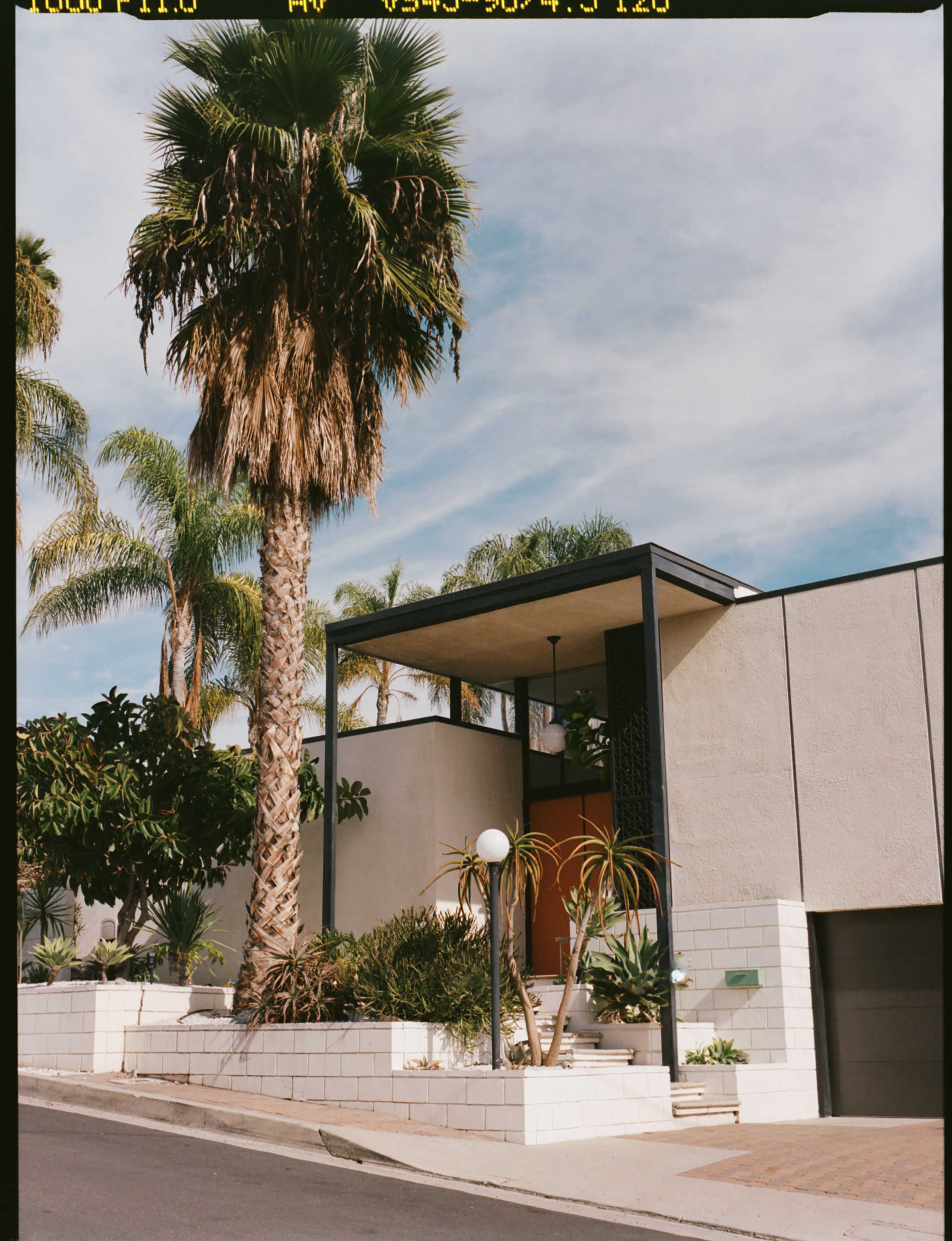 The image shows a modern house with a palm tree in front and a landscaped yard.