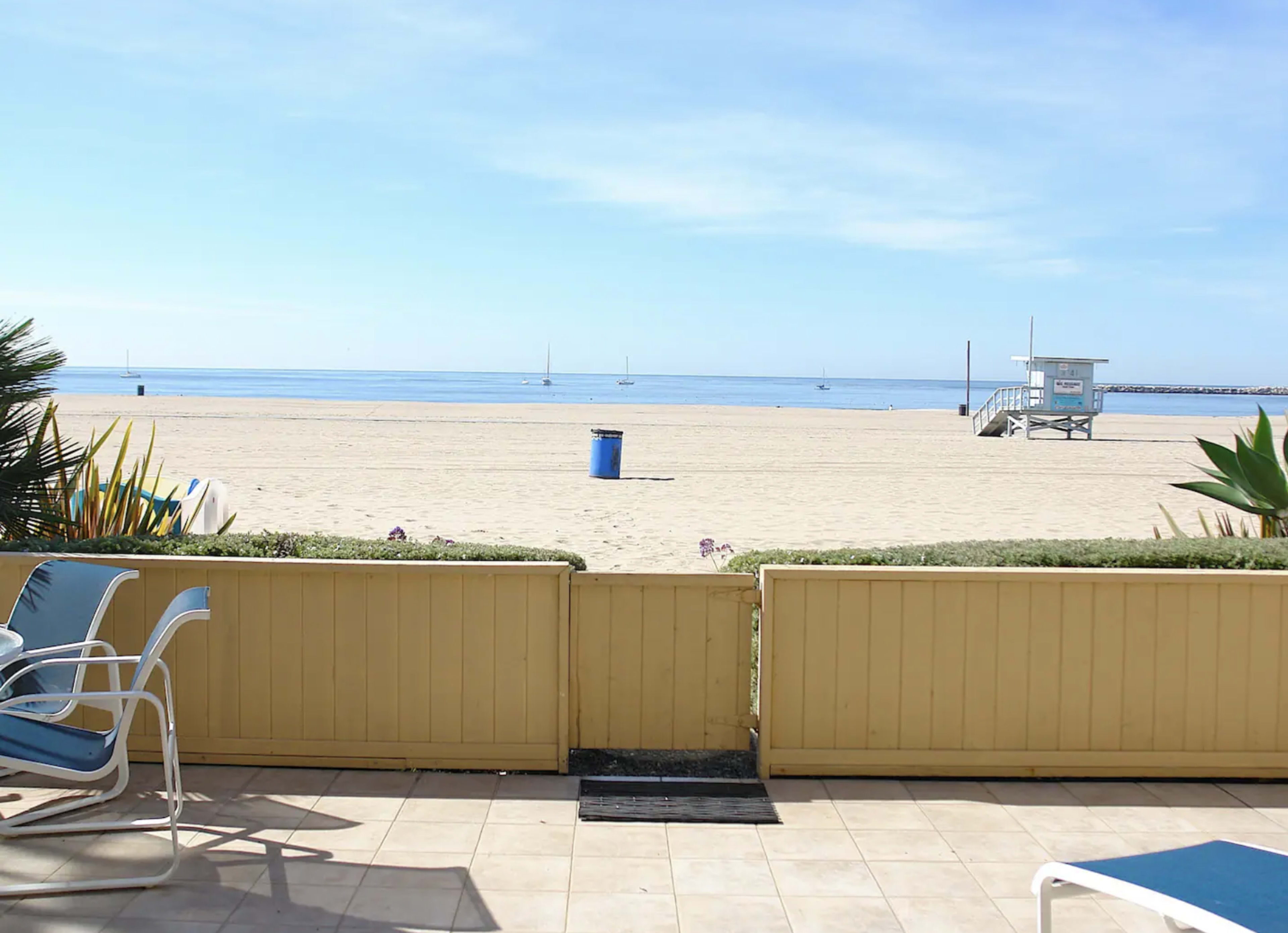 A view of a sandy beach with boats in the distance and a lifeguard tower on the shore.