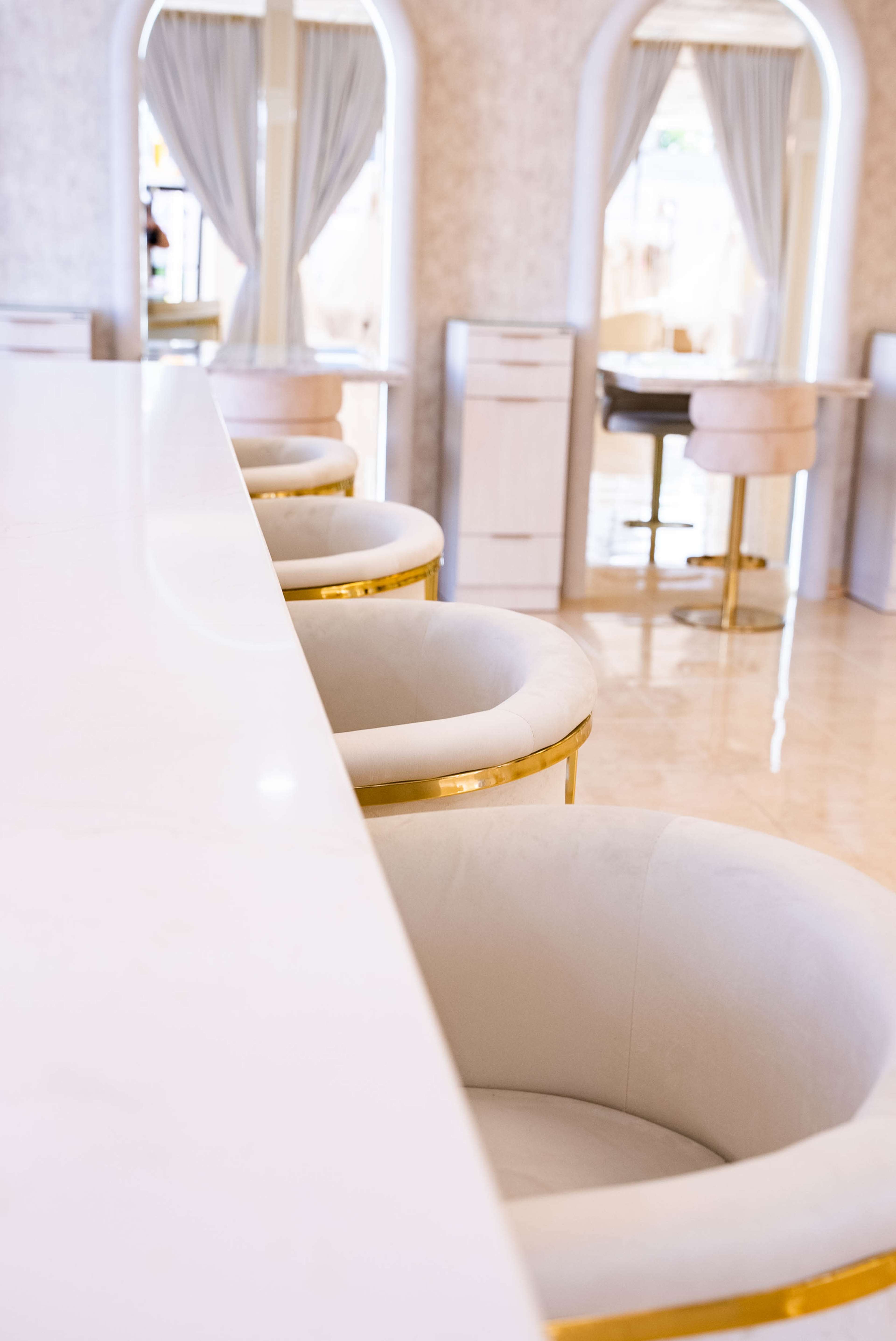 A modern, minimalistic interior featuring white marble countertops and plush, circular chairs with gold accents.