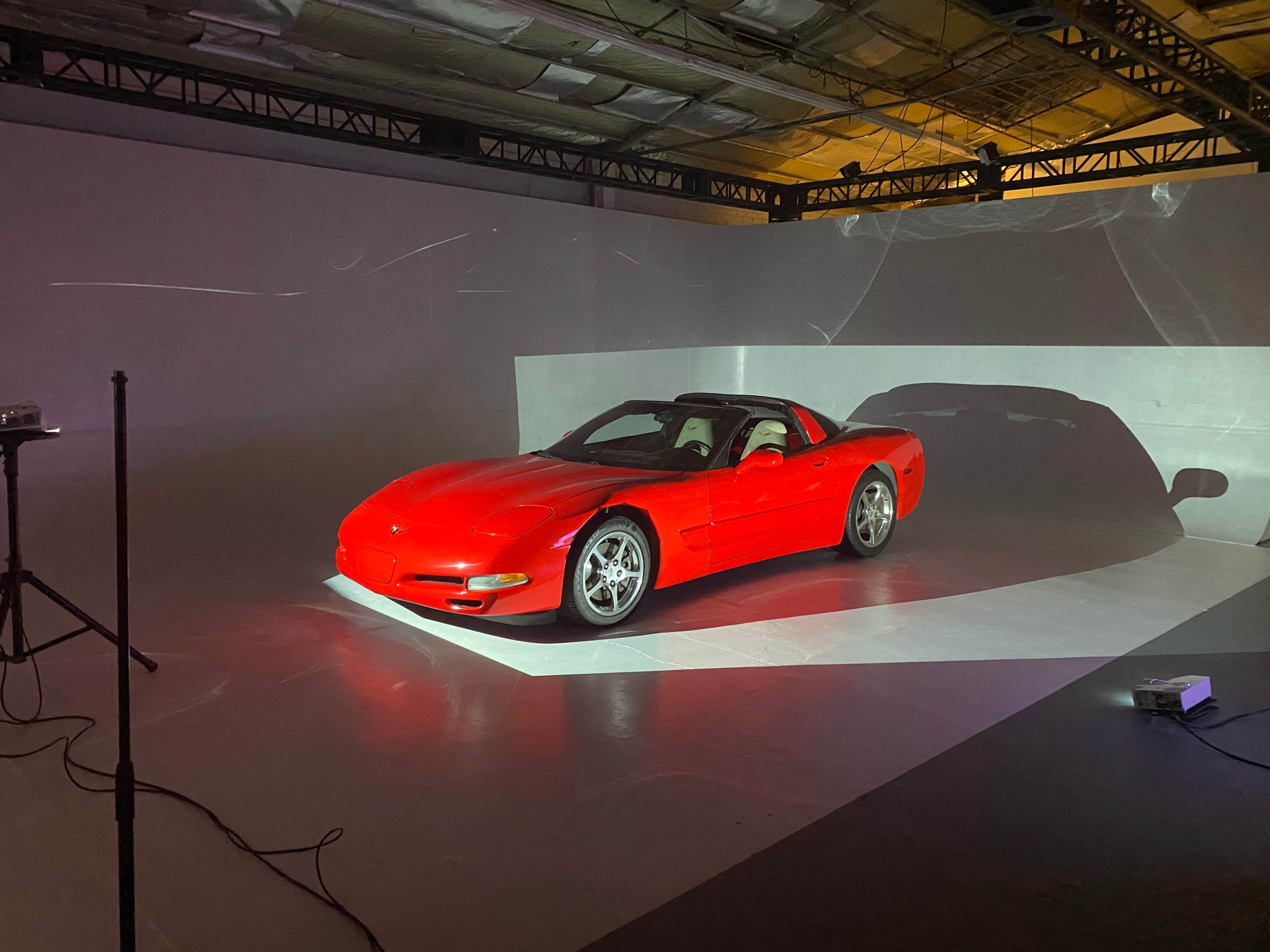 A red sports car is positioned on a white stage with dramatic lighting in a minimalist studio setting.
