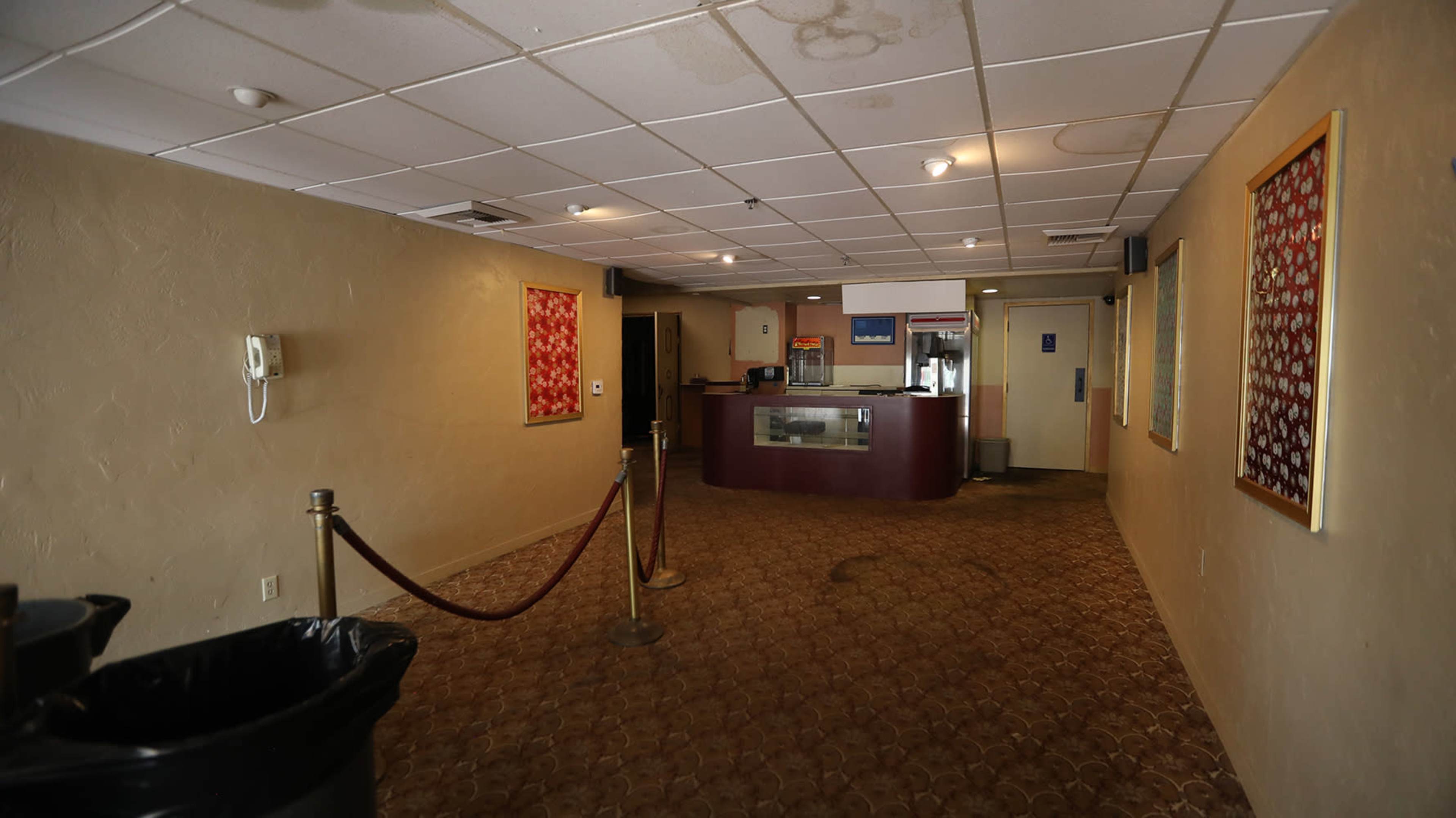 A dimly lit hallway leading to a counter with a cash register, flanked by artwork on the walls and a trash can in the foreground.