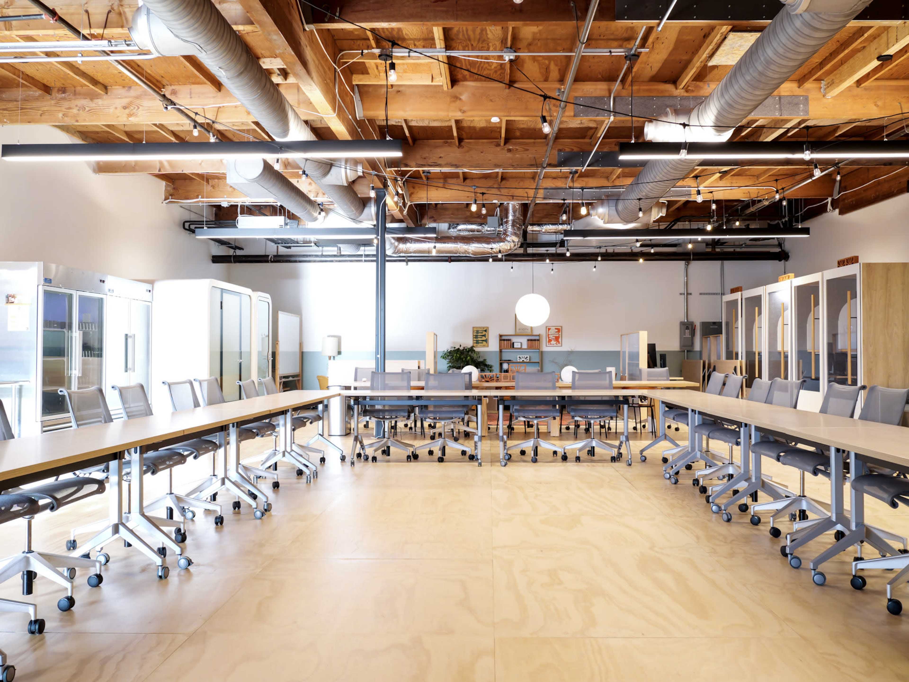 The image shows a spacious modern conference room with a long table surrounded by office chairs, large windows, and soundproof phone booths along the walls.
