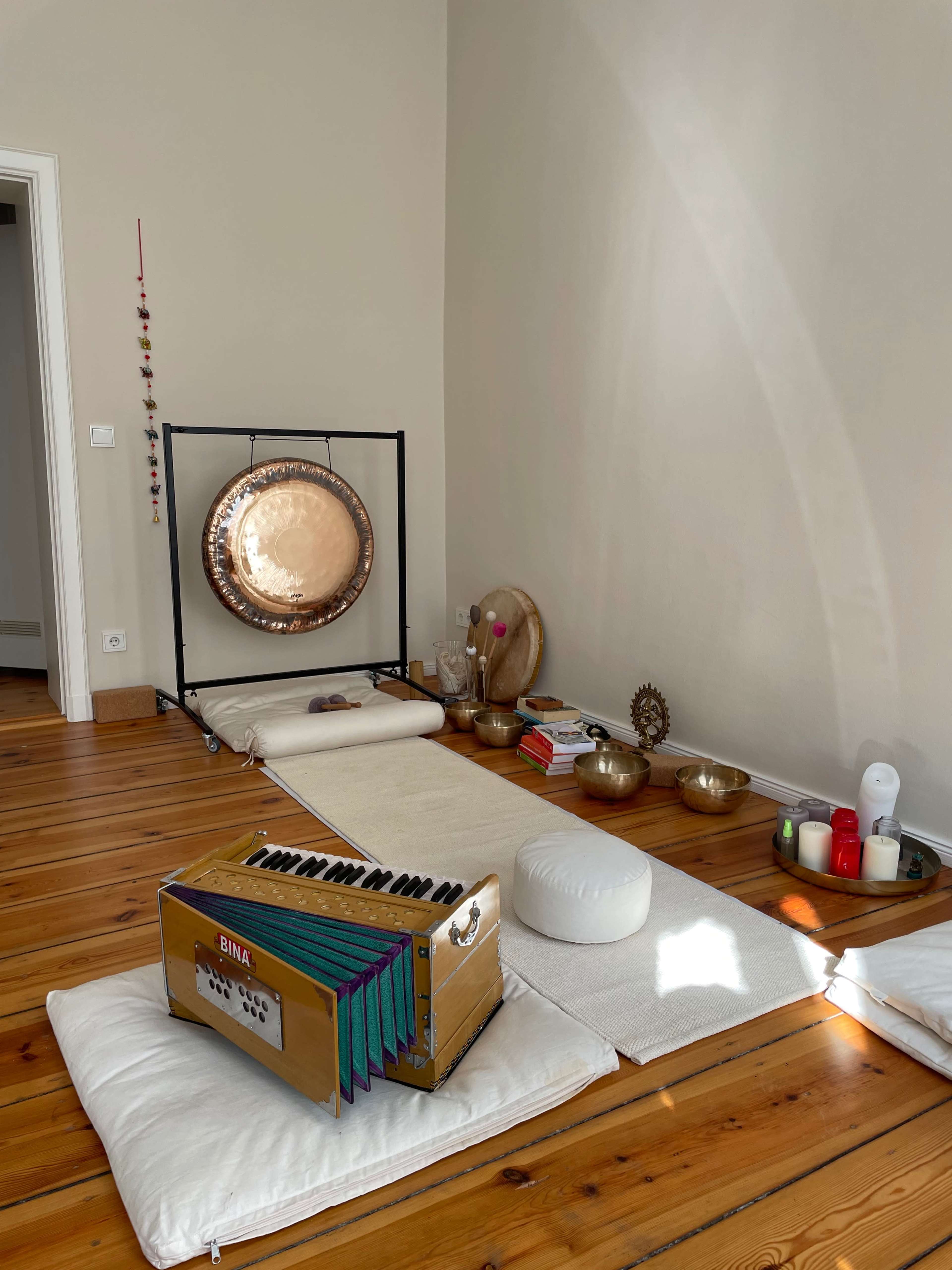 A tranquil indoor space with a large gong, meditation cushions, and various decorative bowls arranged on a wooden floor.