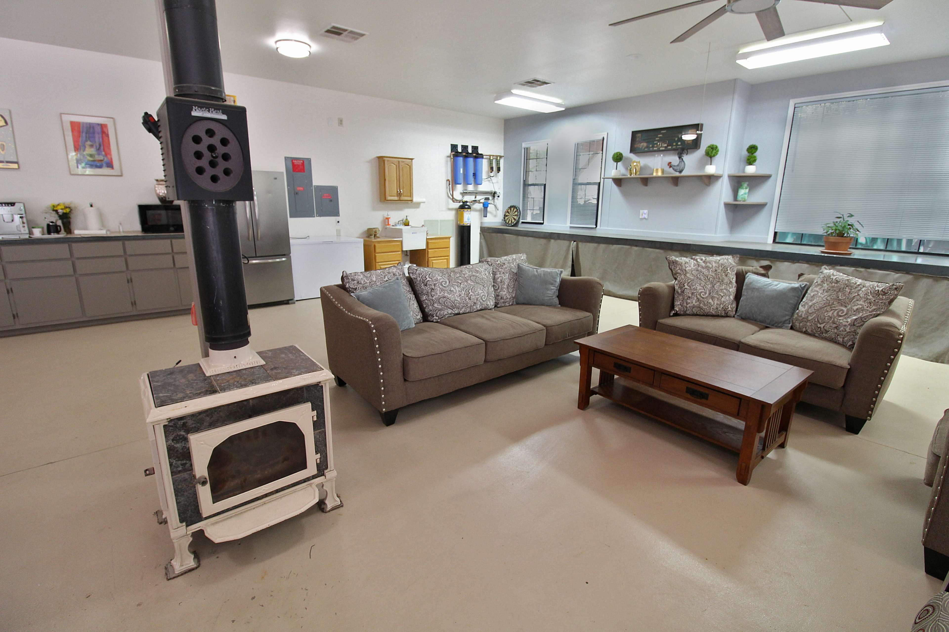 A modern living area features two couches, a wooden coffee table, and a wood stove, with appliances and decorative shelves in the background.