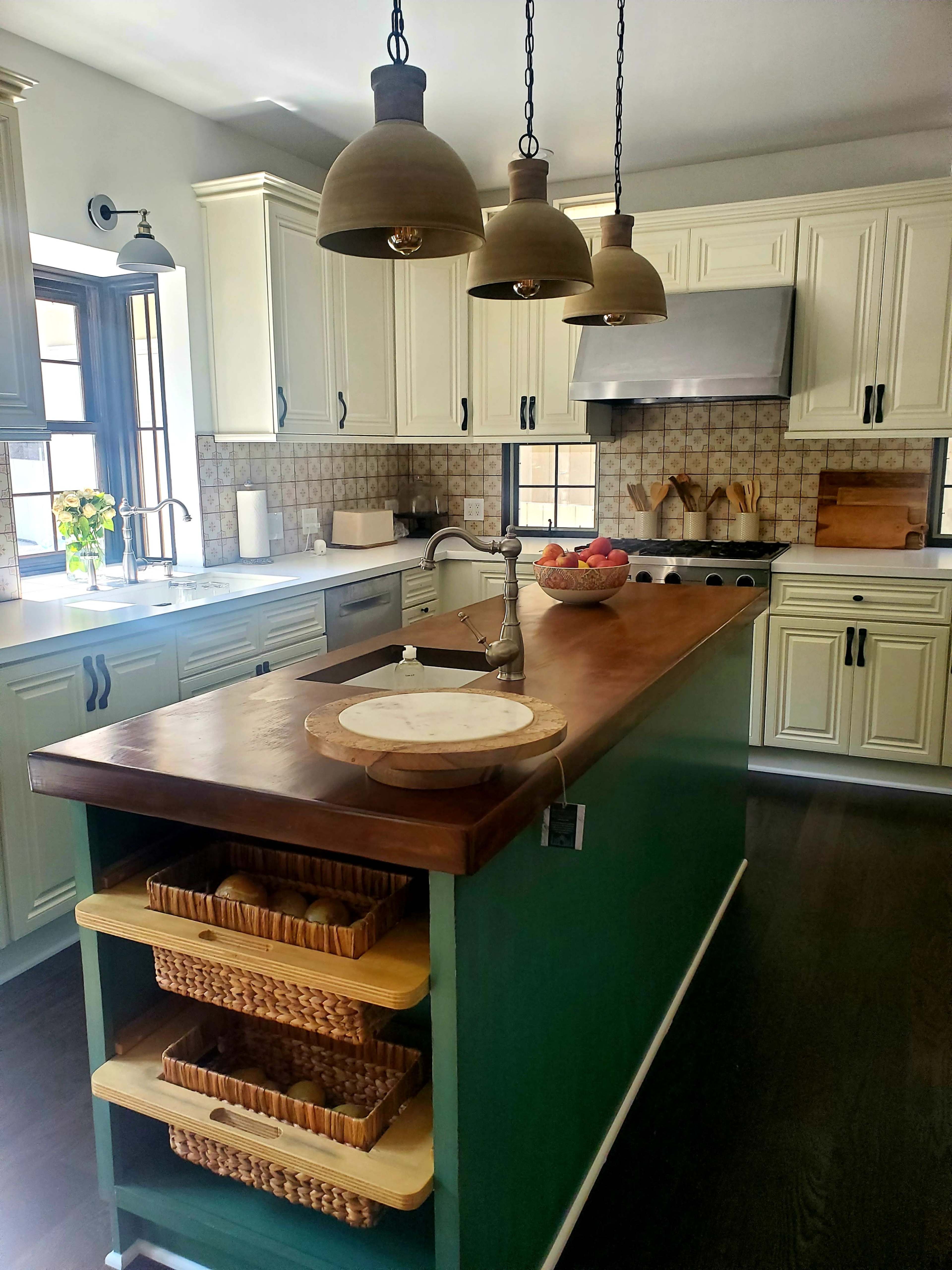 The kitchen features white cabinets, a wooden island with storage baskets, and pendant lights hanging above the countertop.