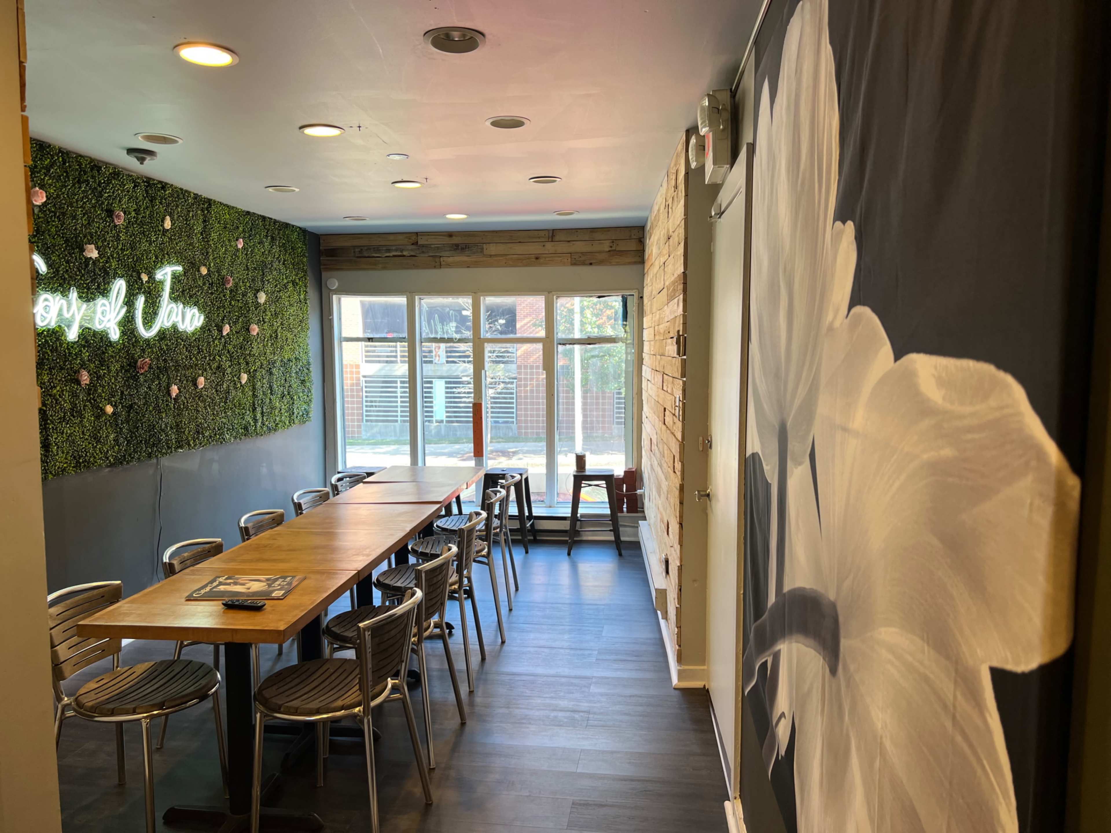 A dining area with a long wooden table and metal chairs, decorated with a green wall of plants on one side and large flower artwork on another.