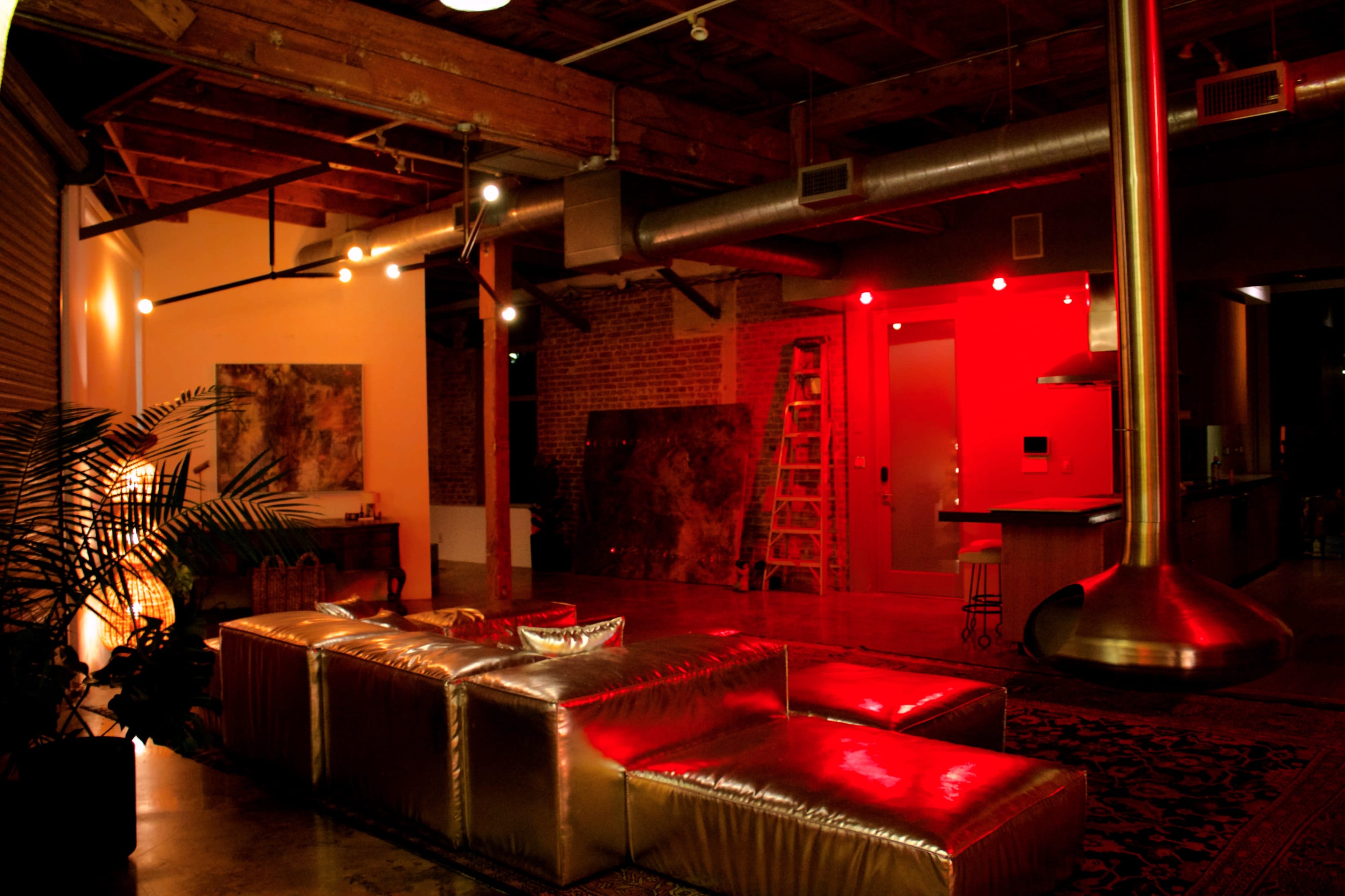 The image shows a modern living space with a metallic sofa, exposed wooden beams, and red accent lighting.