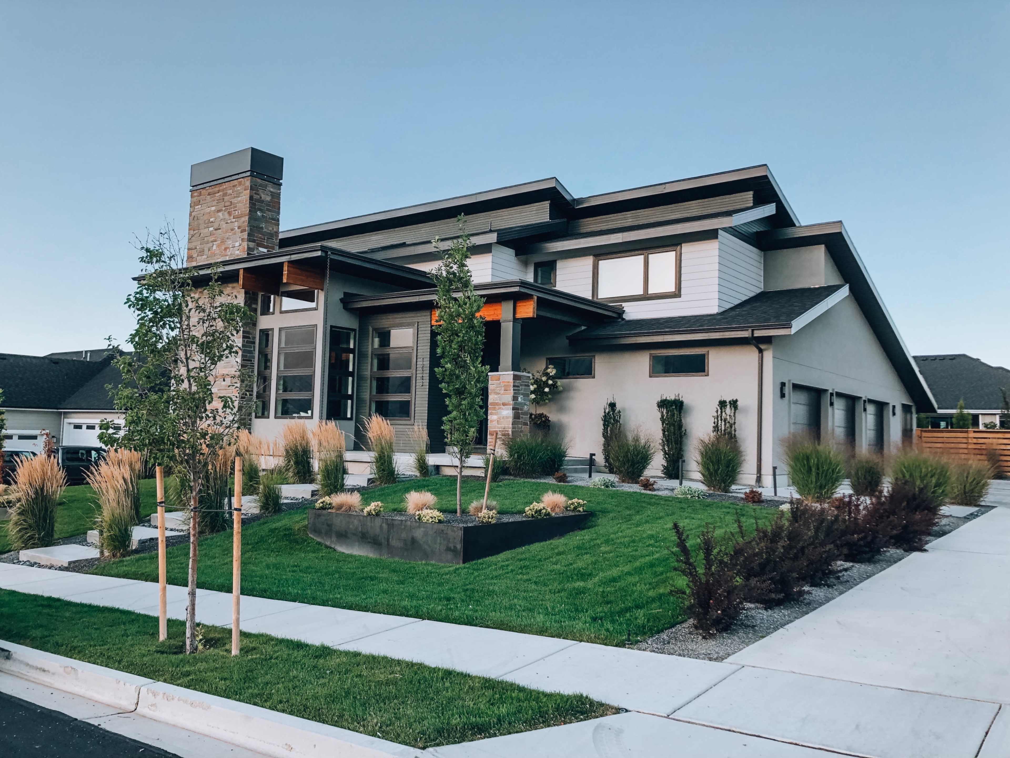 A modern house features a combination of stone and wood elements, with a landscaped yard and a three-car garage.