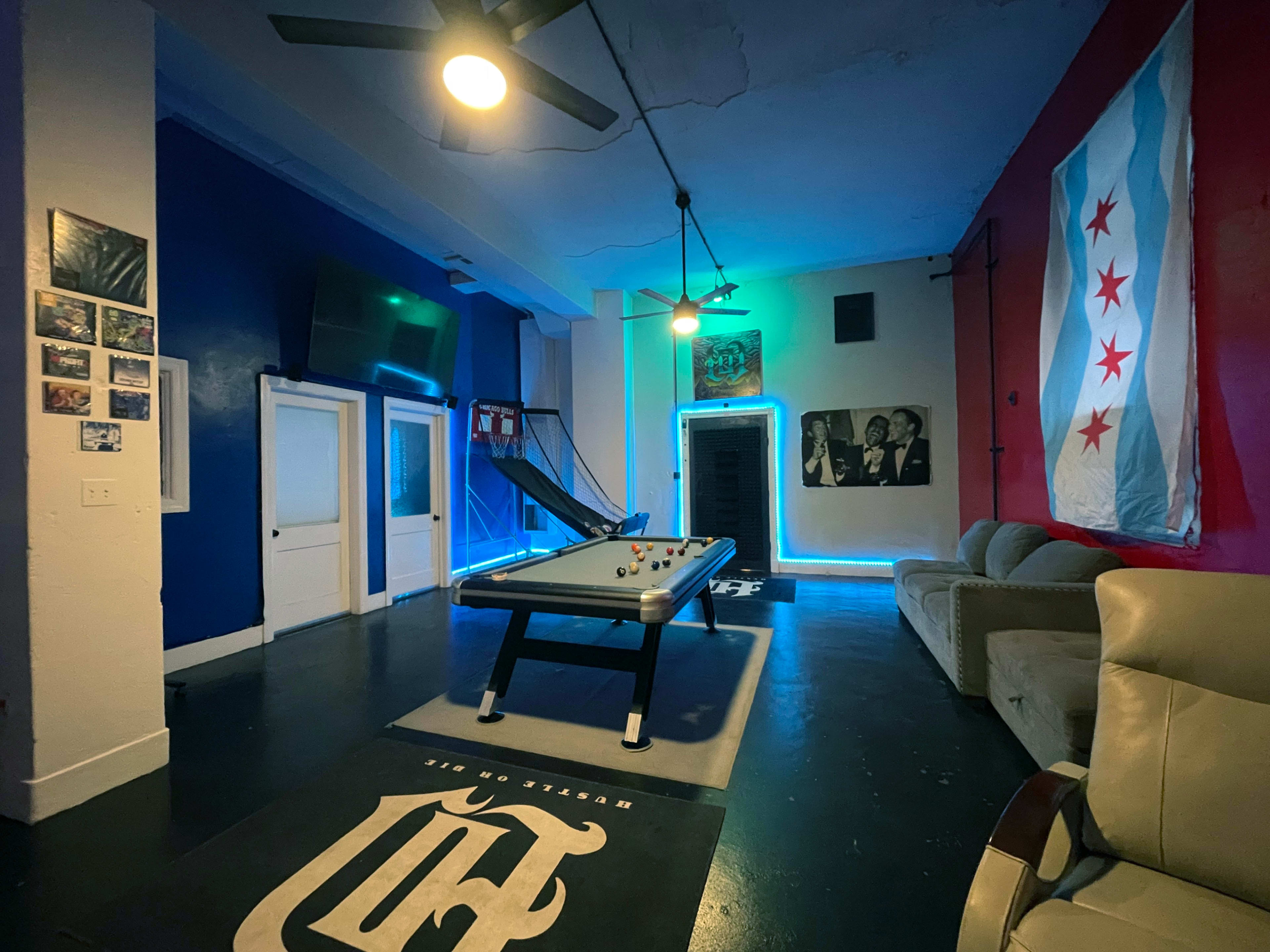 The image shows a recreational room featuring a pool table, a Chicago flag on the wall, and modern lighting accents.