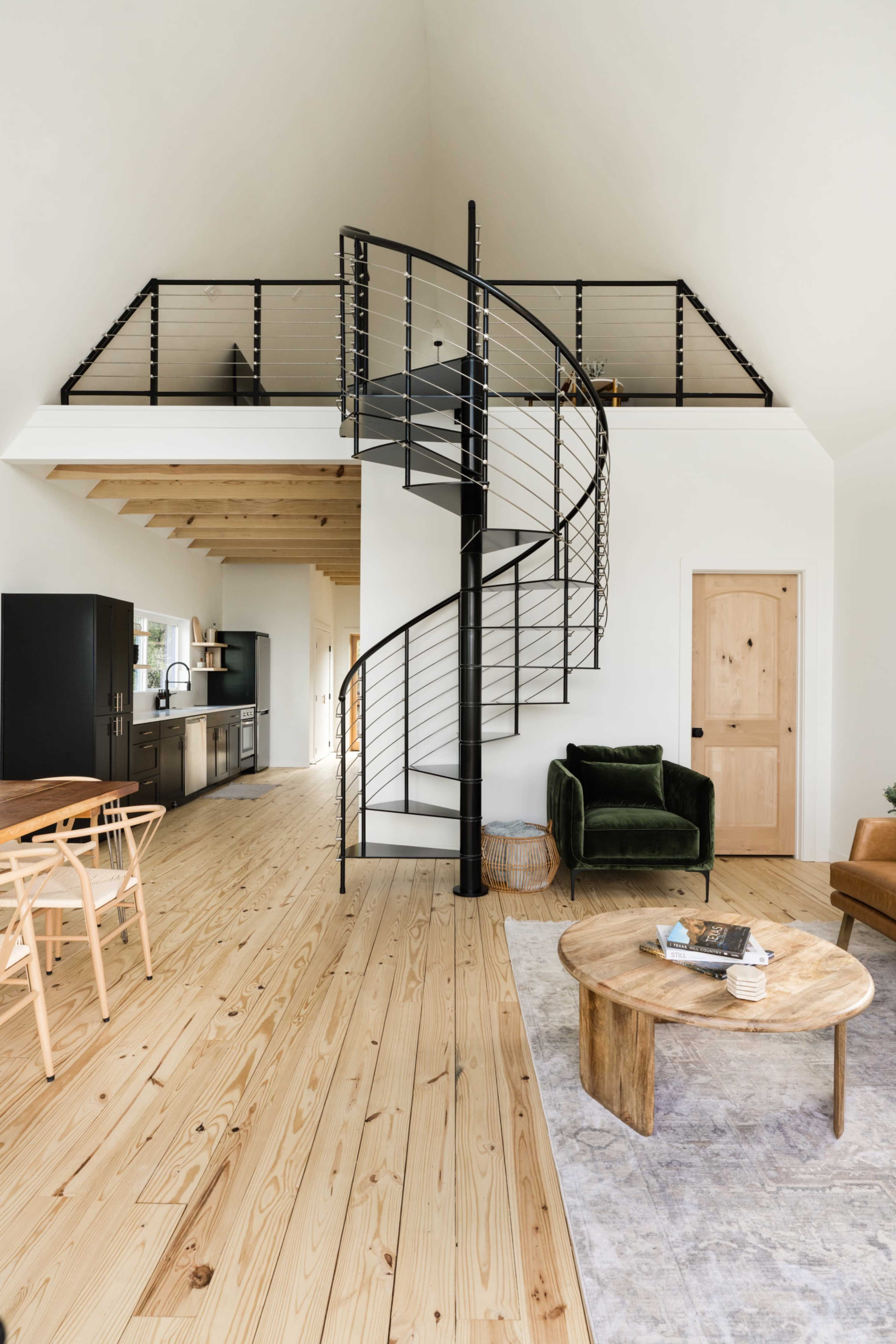 A modern interior with a spiral staircase leading to an upper level, featuring a wooden floor, a black kitchen, and a cozy seating area.