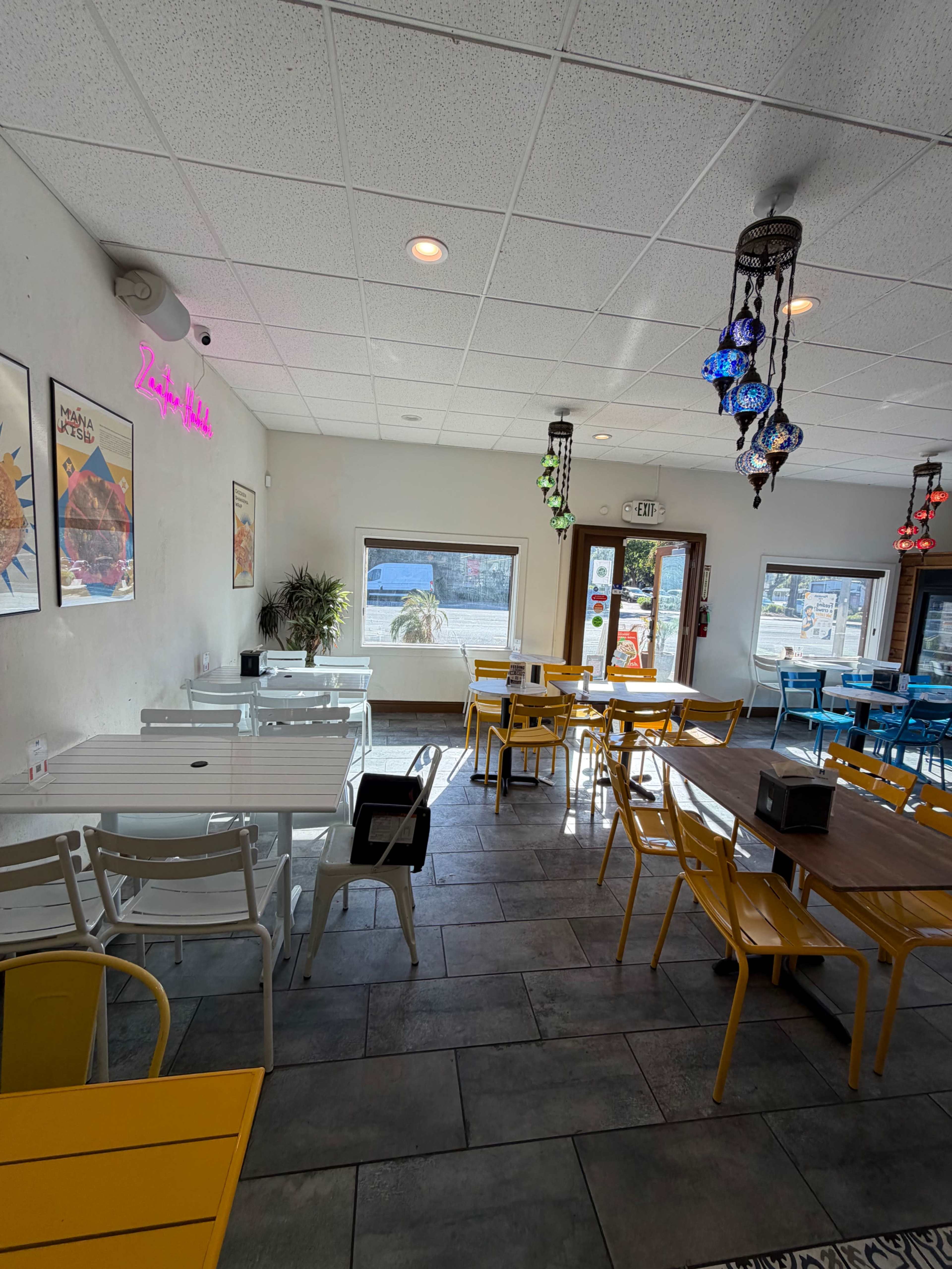 The interior of a brightly colored restaurant features a mix of white and yellow tables, with decorative hanging lights and a view of the outdoors through large windows.