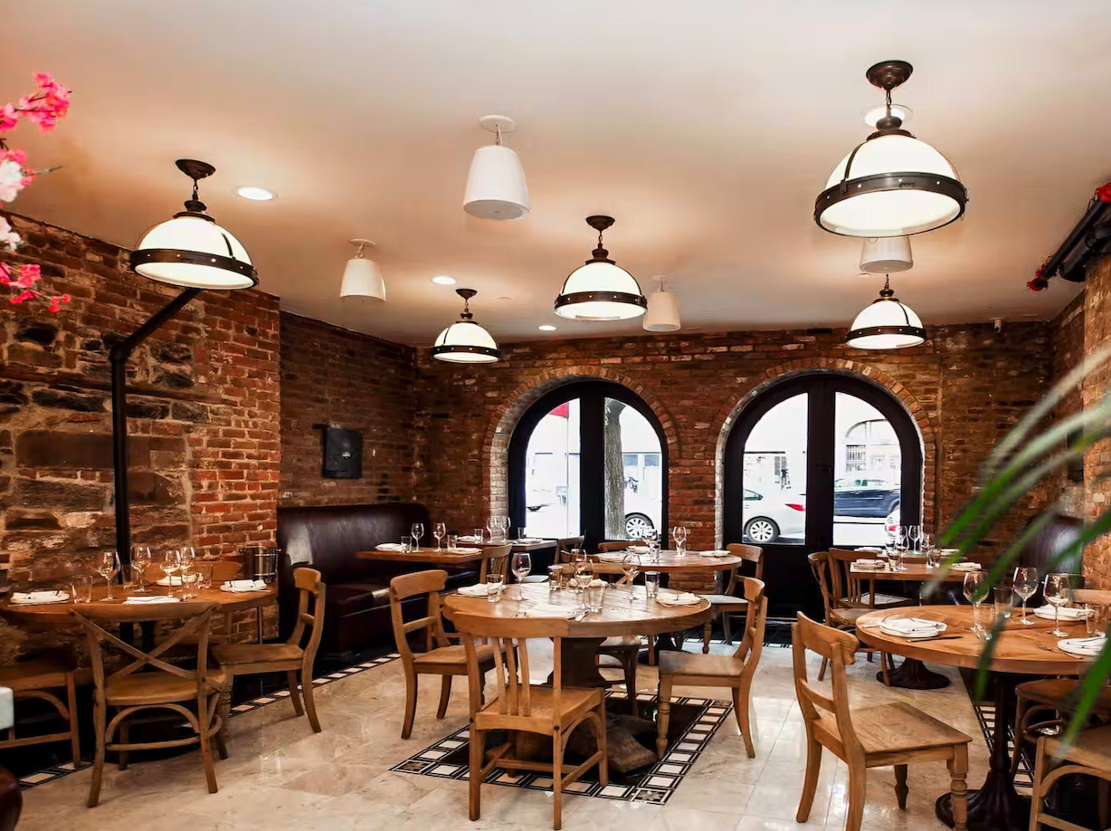 The image shows a rustic restaurant interior with exposed brick walls, arched windows, wooden tables, and various light fixtures.