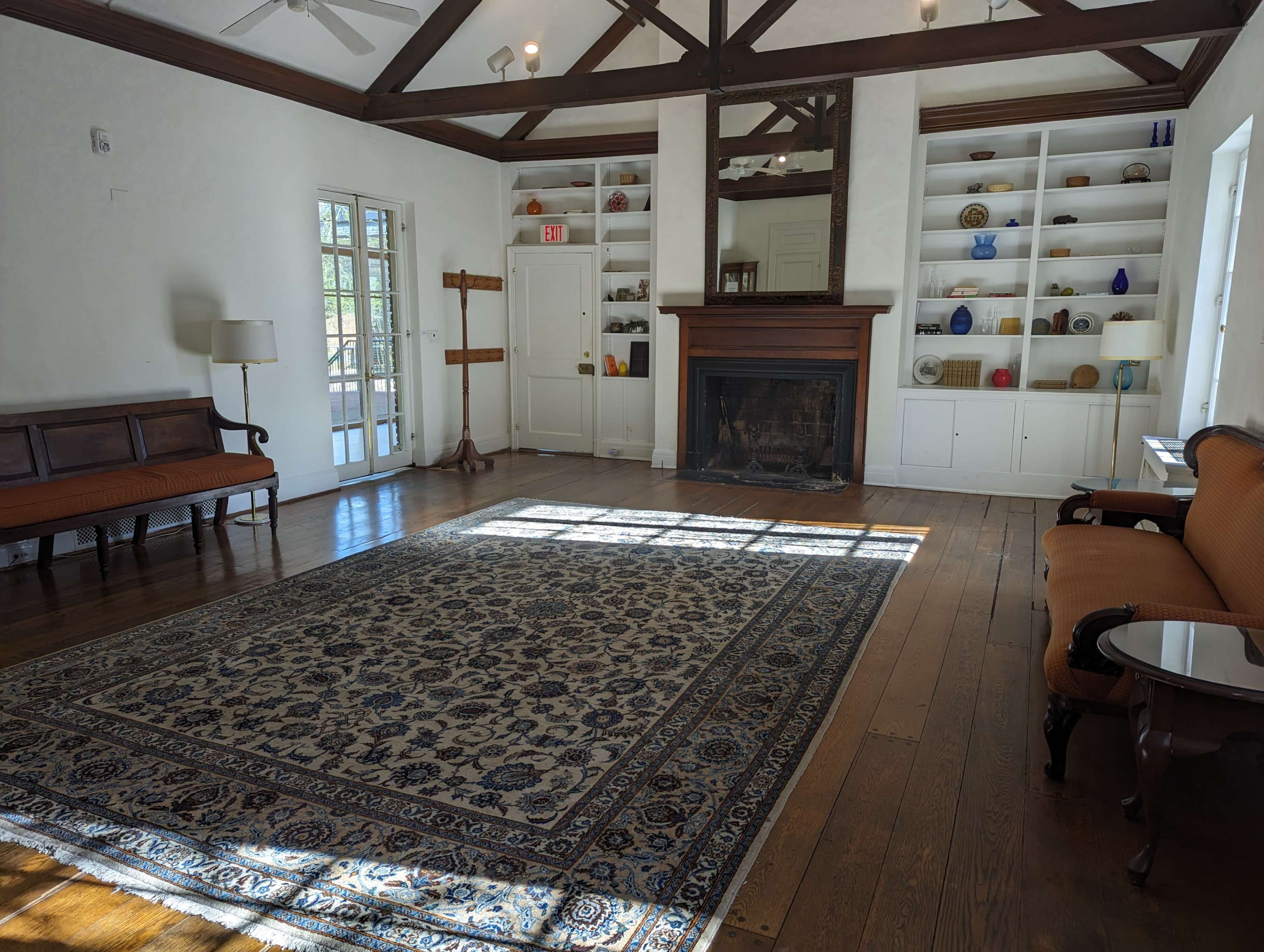 A brightly lit room with wooden floors, a large area rug, two sofas, and shelves displaying decorative items.